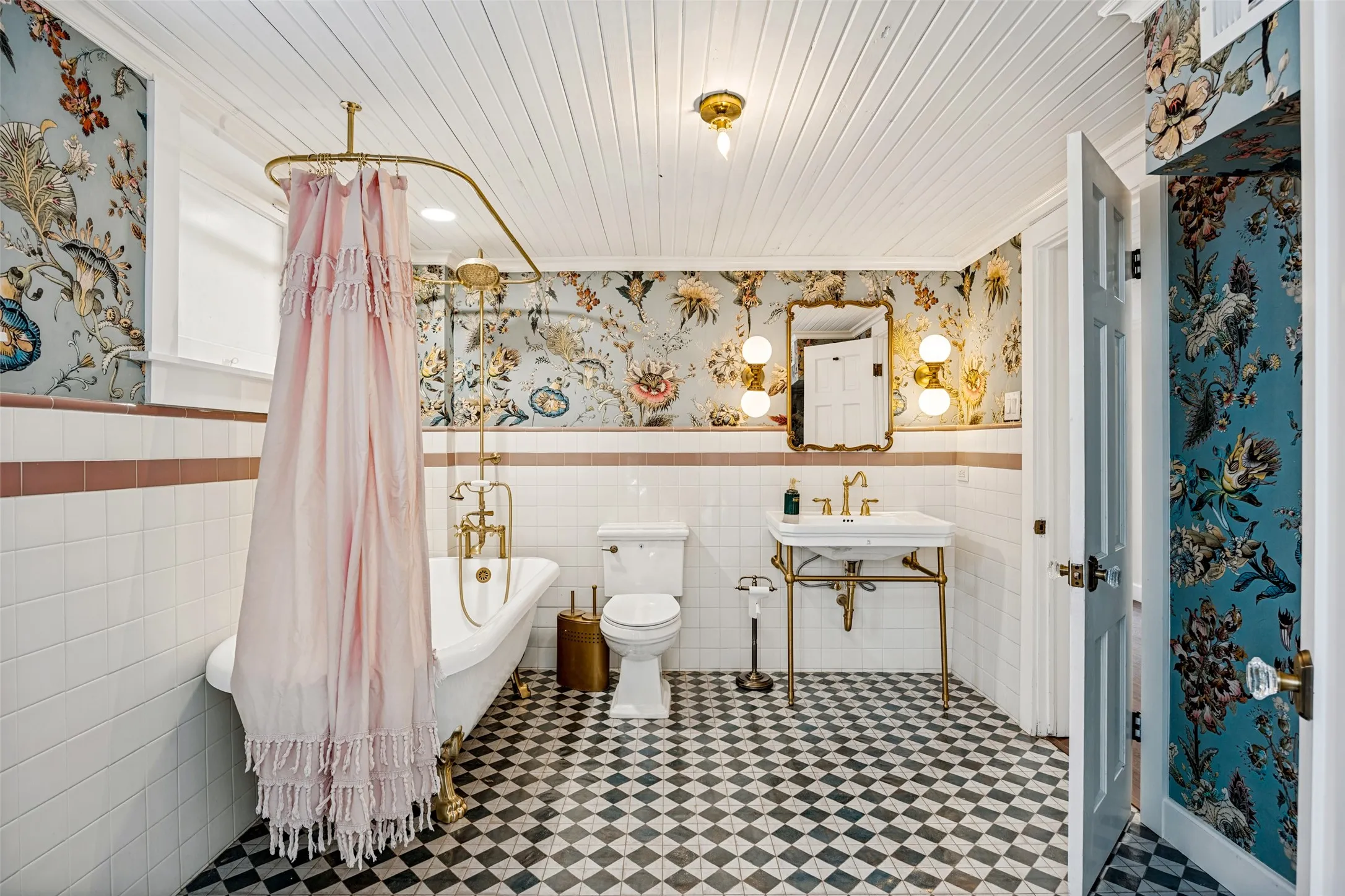 Clawfoot bathtub with brass fixtures, pedestal sink with brass frame, patterned floor tiles, shiplap ceiling, and ornamental wall coverings