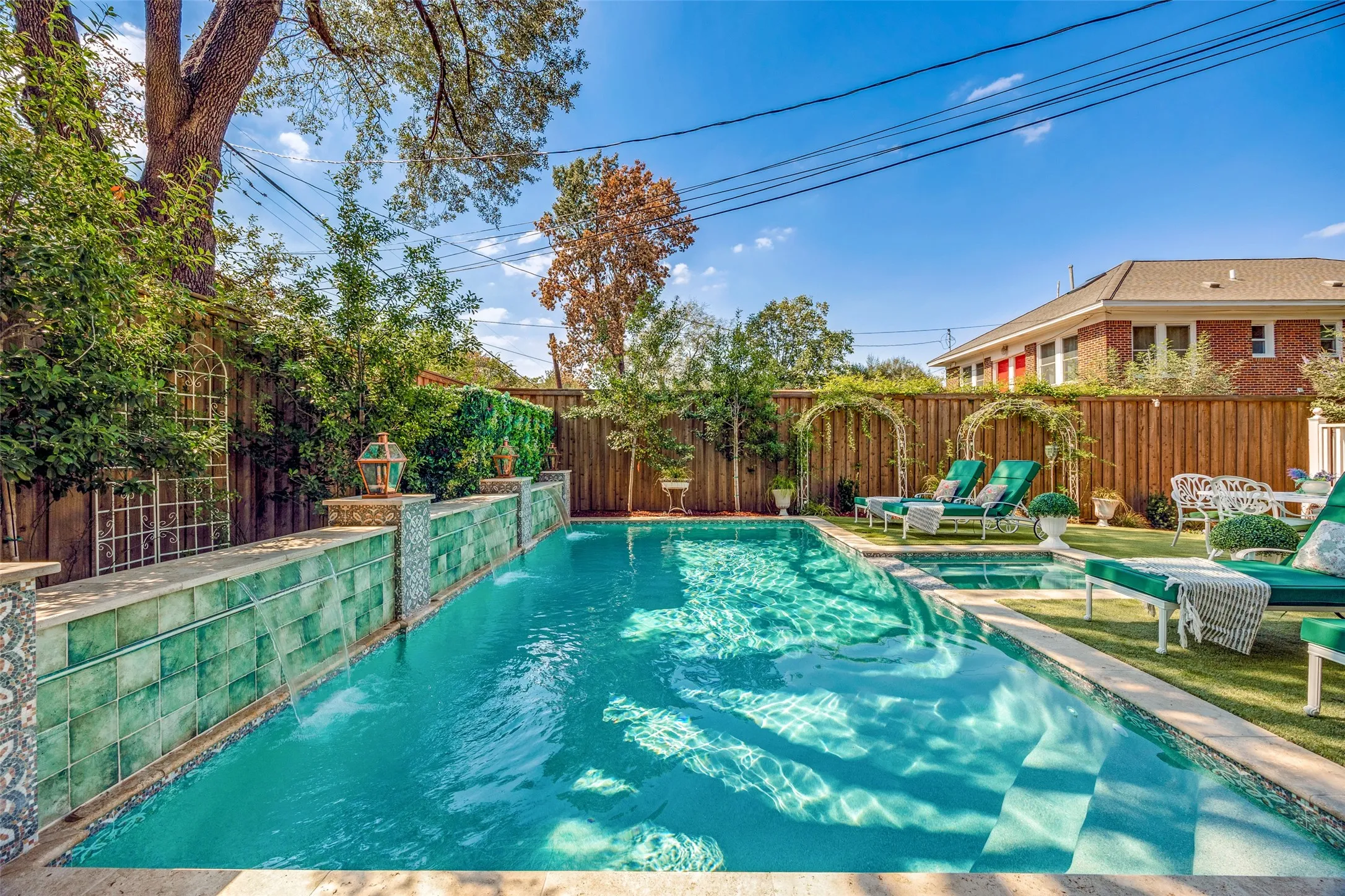 Swimming pool with integrated spa, waterfall feature, artificial turf surround, and wooden privacy fencing