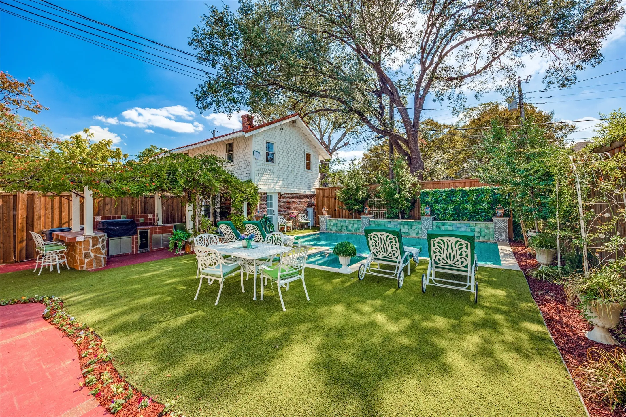 Outdoor entertaining area with artificial turf, an integrated outdoor kitchen, a swimming pool with decorative tile, and a privacy fence