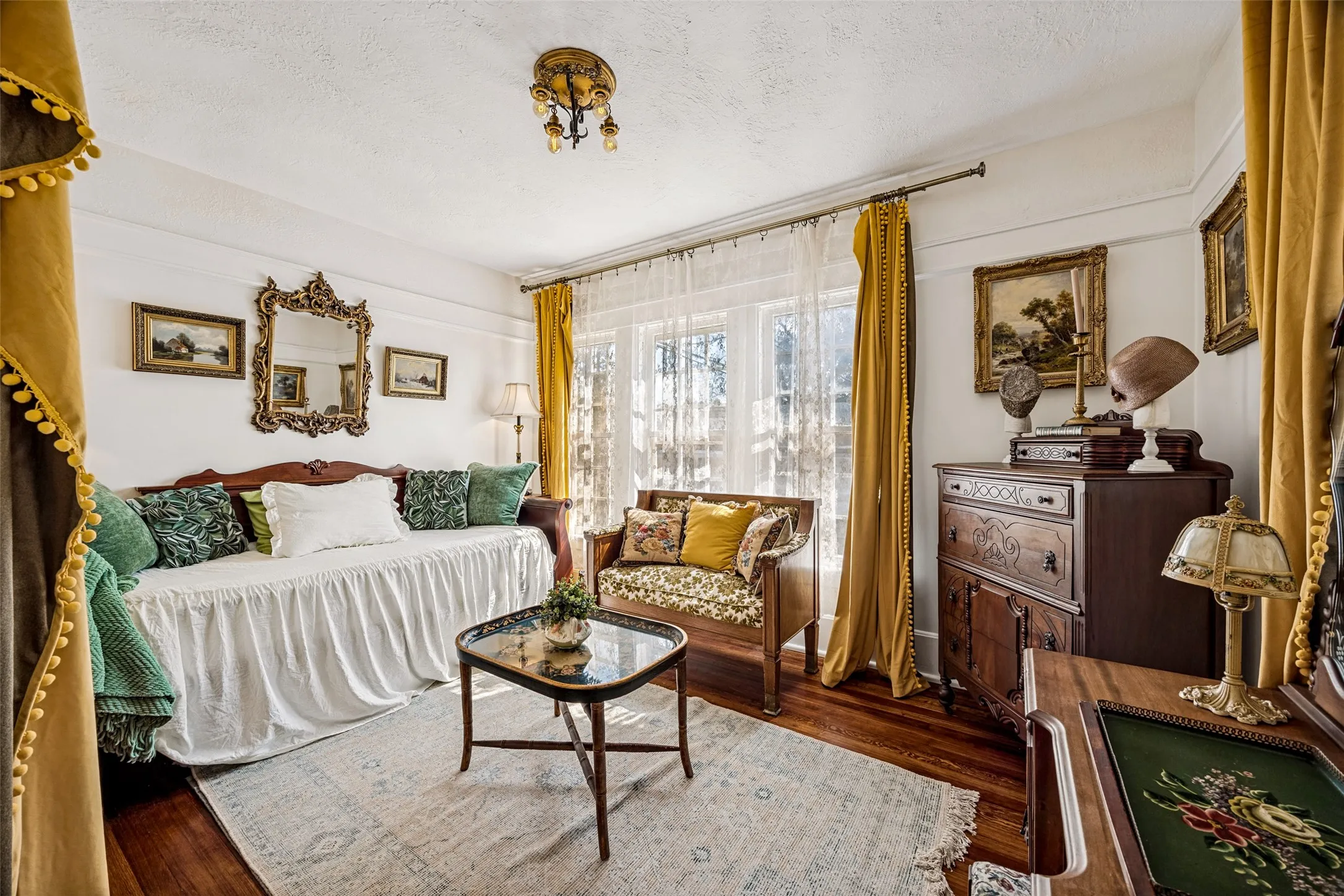 Hardwood flooring, ornate ceiling light fixture, white walls, large window with sheer and solid drapes, decorative wall mirror