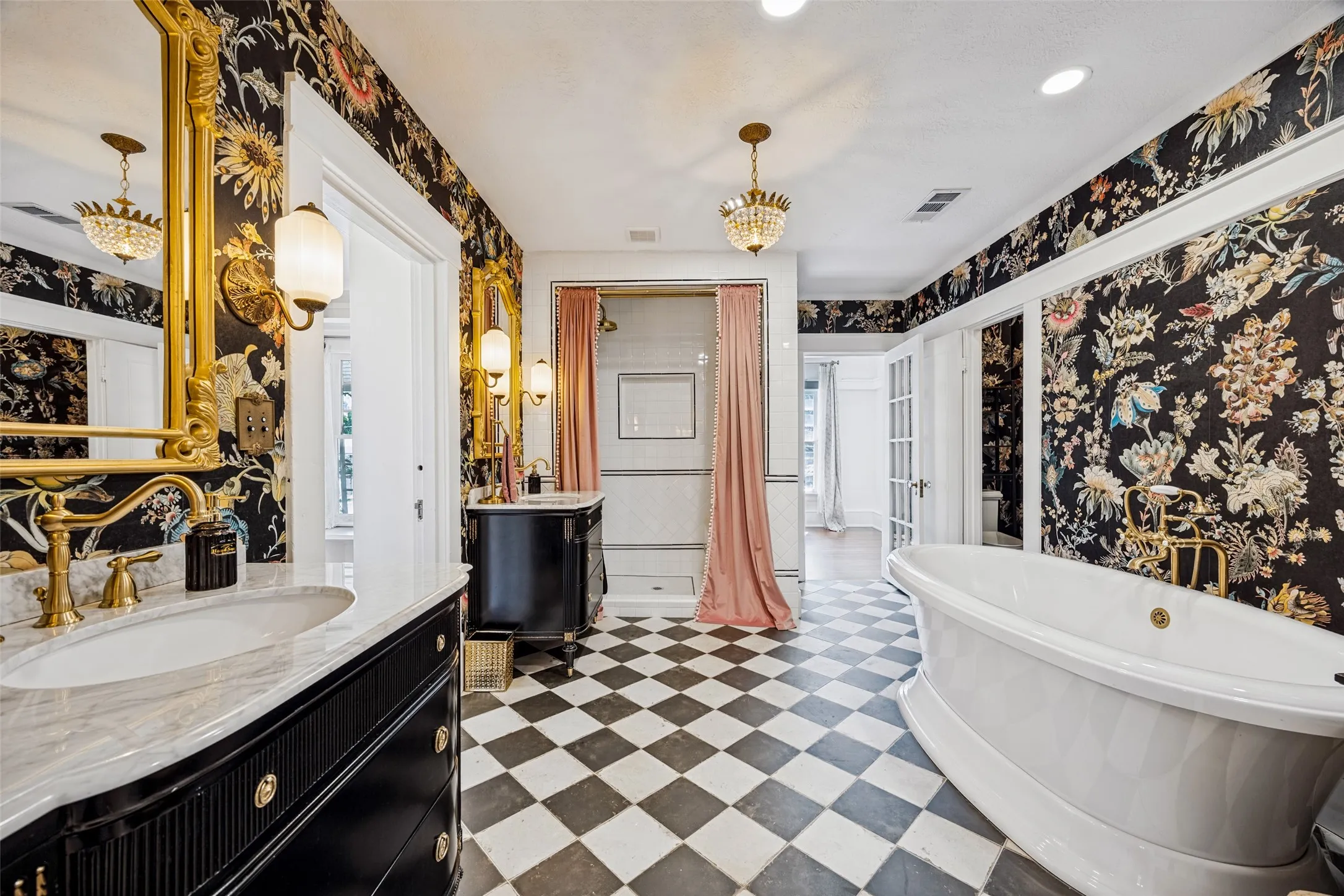 Black and white checkered tile flooring, ornate gold-framed mirrors, free-standing soaking tub, built-in vanity with marble countertop, and a glass-enclosed shower