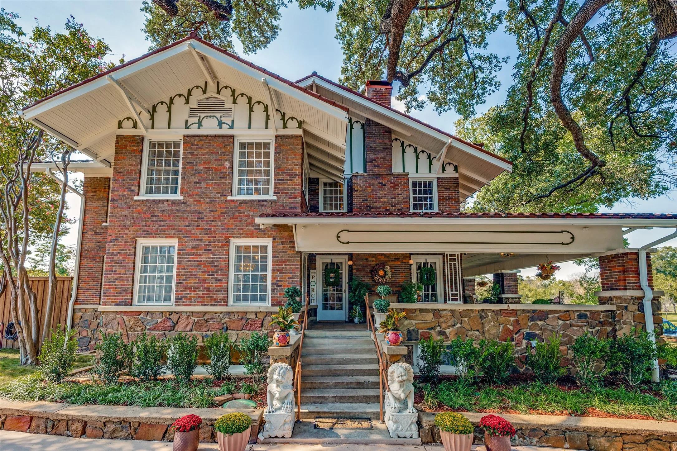 Brick and stone exterior with decorative gable trim, offering a covered porch with stone detailing and mature trees