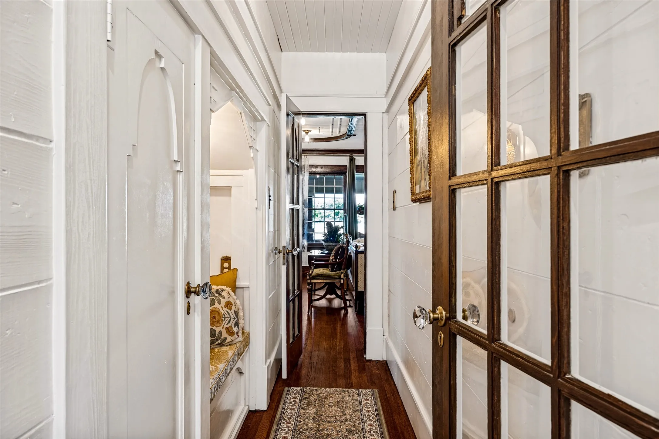 Hardwood flooring throughout, white paneled walls, glass-paned doors, and built-in alcove seating