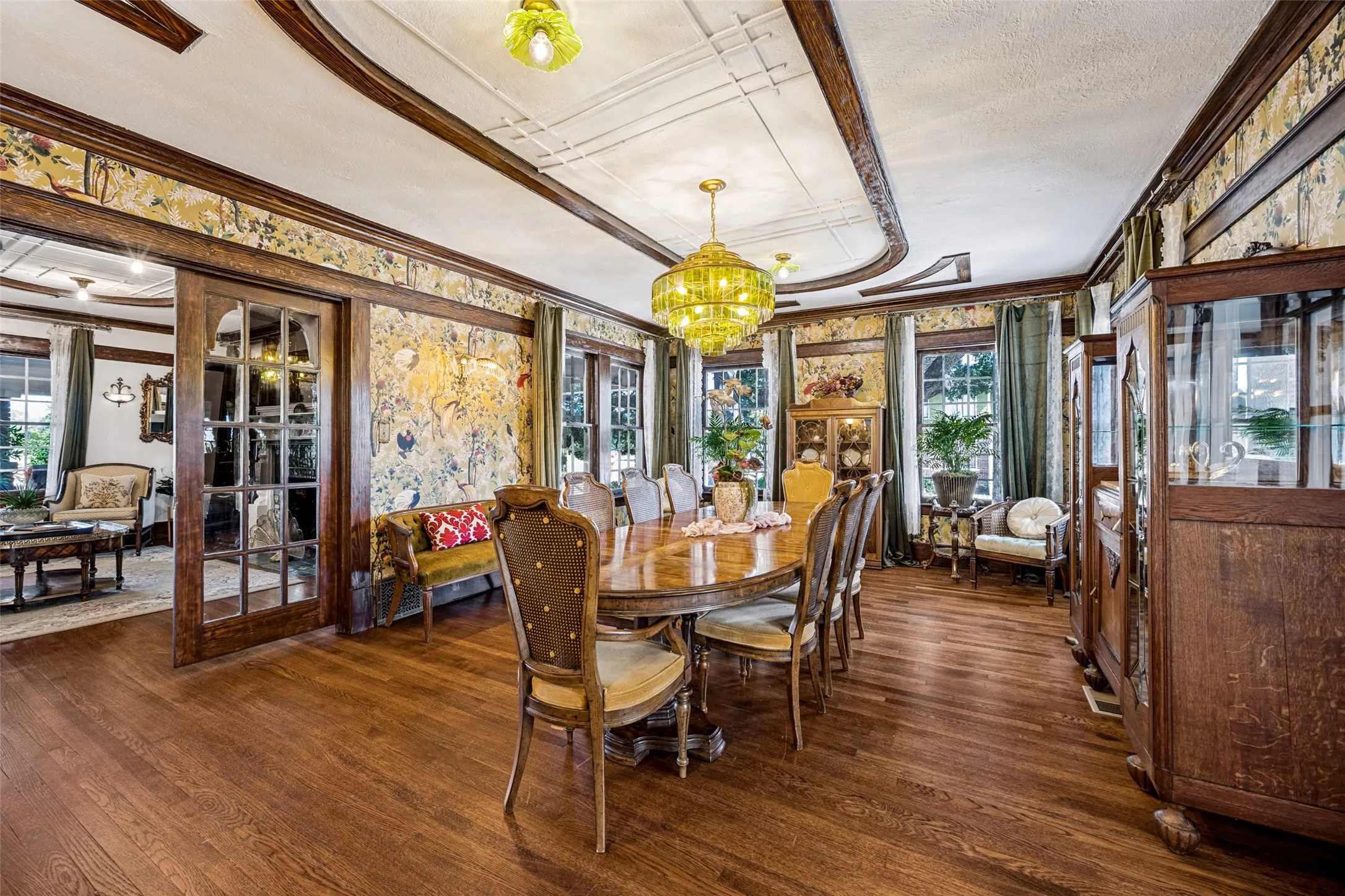 Hardwood flooring, ornate ceiling trim, decorative wall coverings, French doors, and prominent windows with drapery