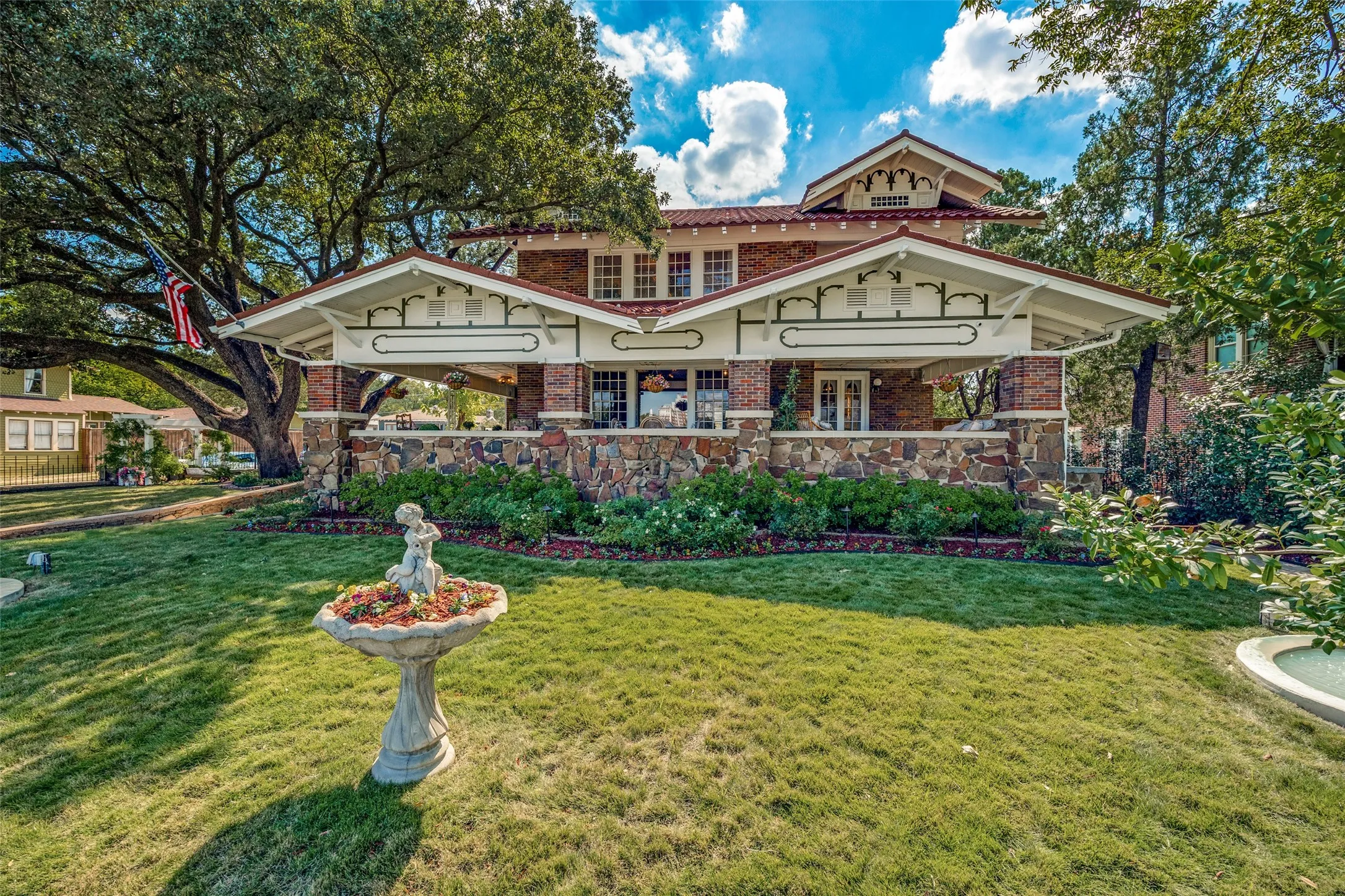 Craftsman-style exterior with brick and stone accents, covered porch, multiple gables, and a mature tree canopy