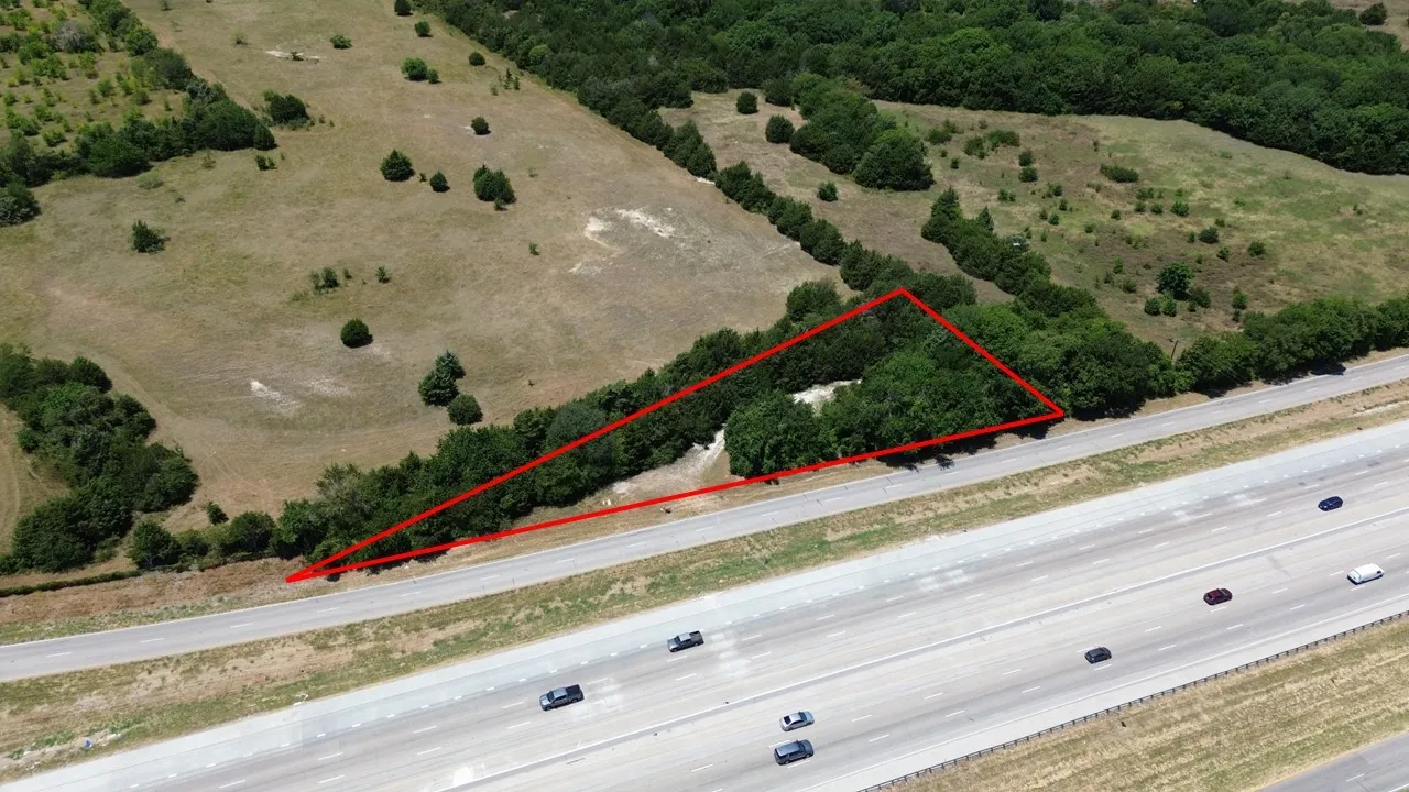 Expansive land parcel featuring natural tree coverage and direct highway frontage