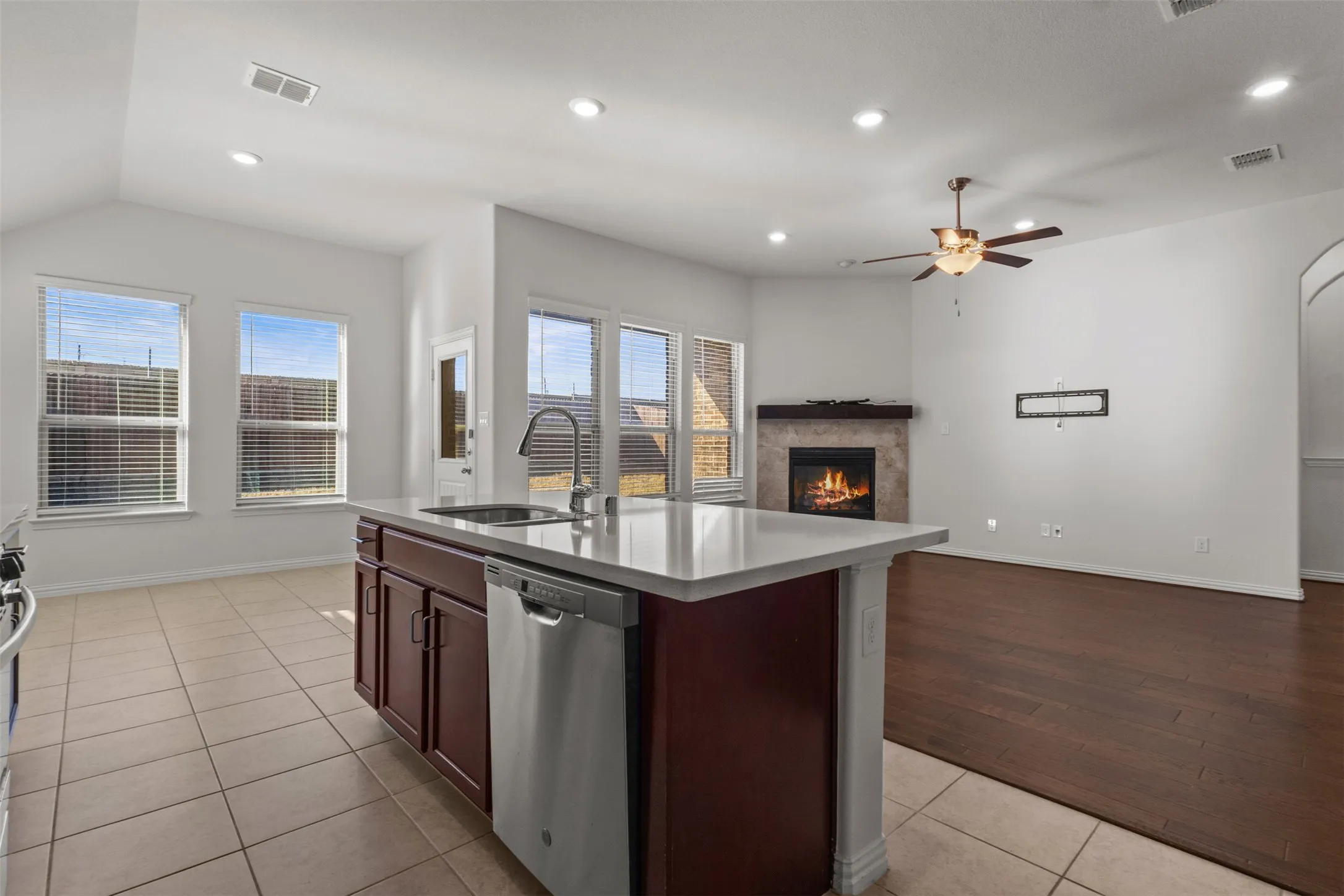 Kitchen island with a built-in sink and stainless steel appliances, tile flooring, recessed lighting, fireplace with a stone surround, and wood-finish flooring