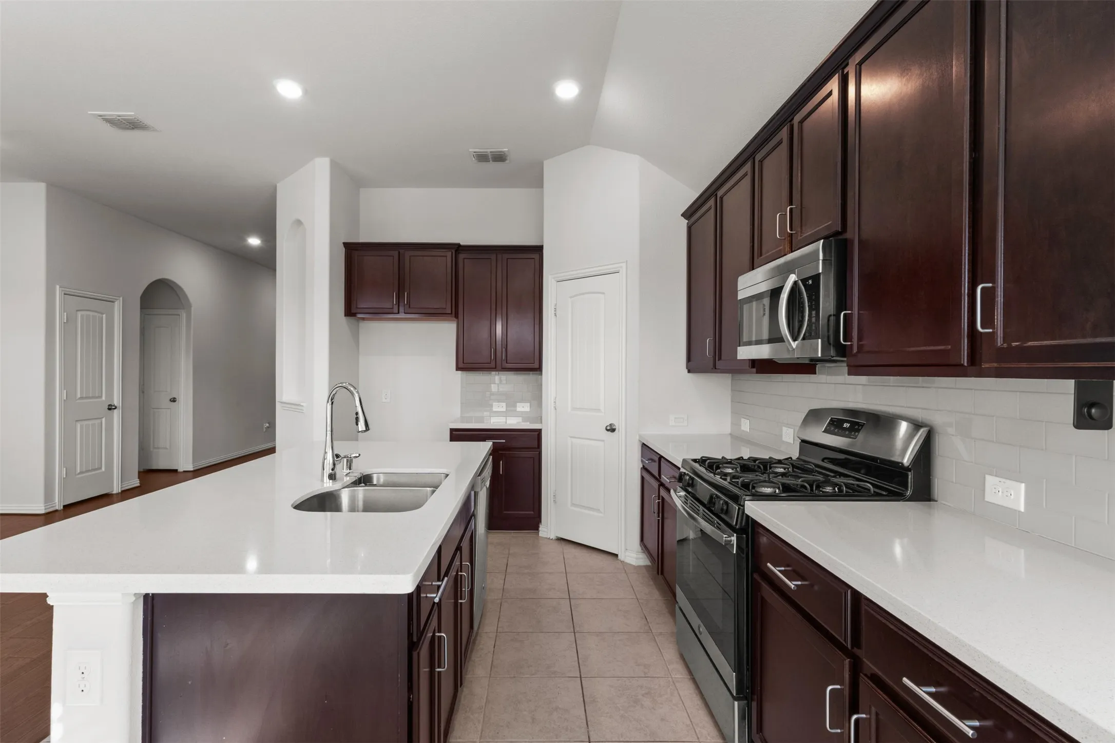 Kitchen featuring dark wood cabinetry, white countertops, stainless steel appliances, and a subway tile backsplash
