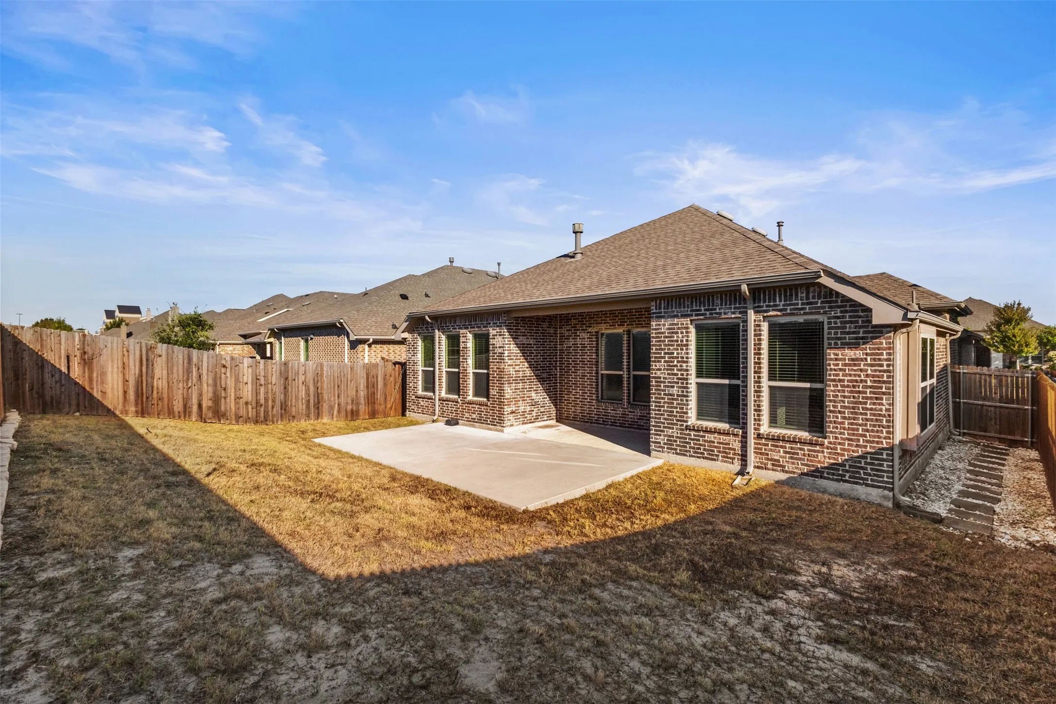 Brick exterior with multiple windows, covered concrete patio, and a fenced backyard