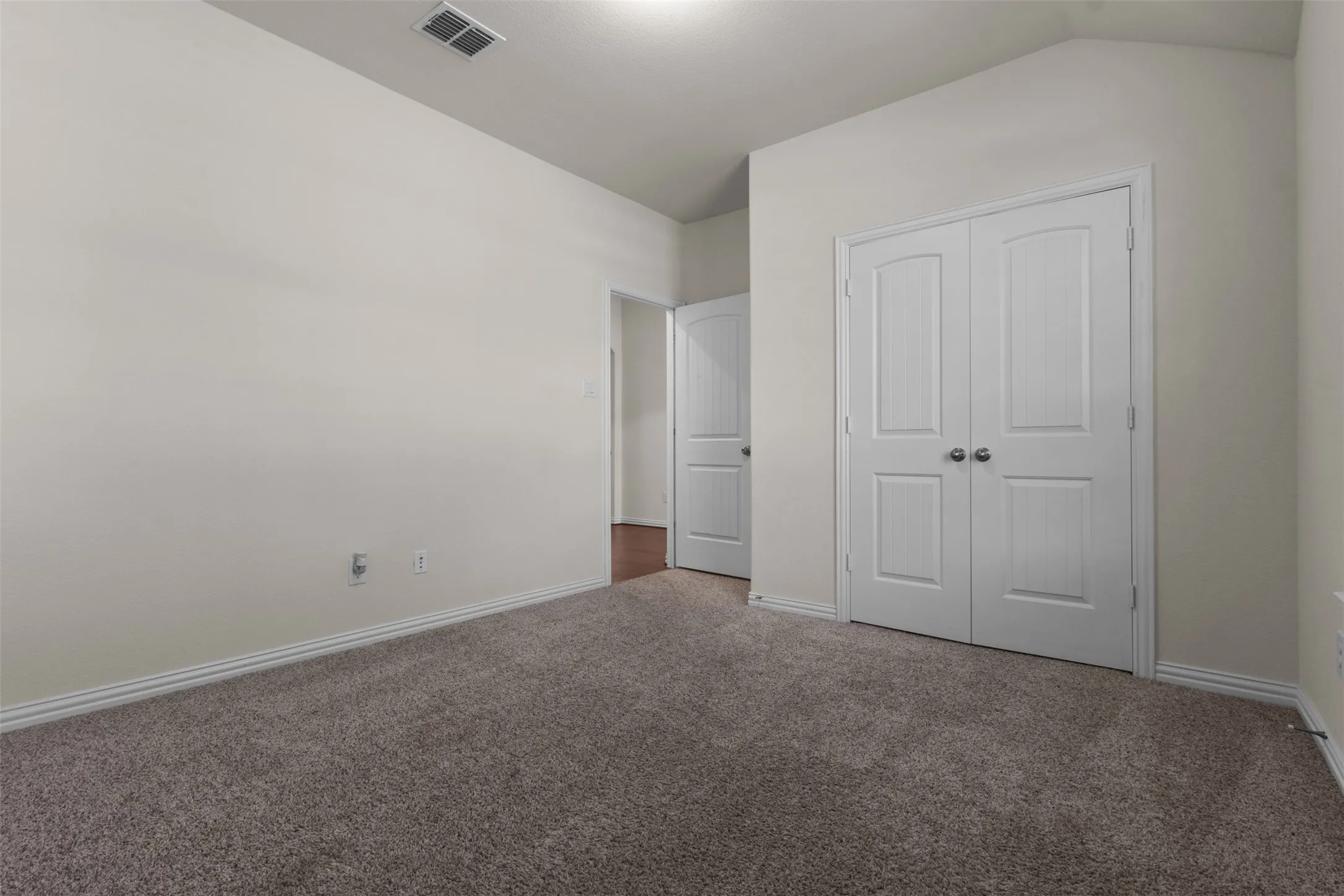 Carpeted room featuring white walls and a double-door closet with arc paneling