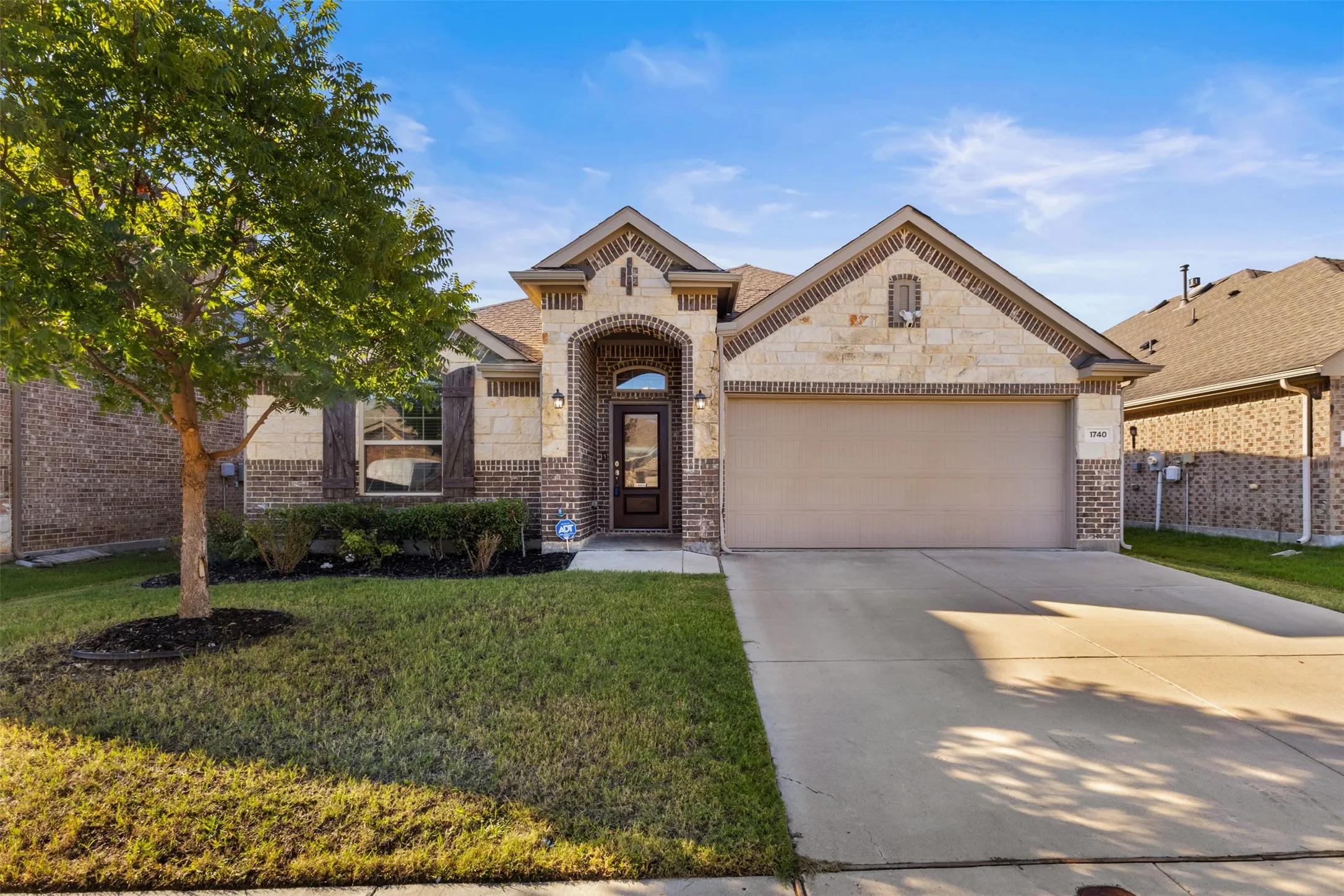 Brick and stone exterior with an arched entryway, attached garage, concrete driveway, and front landscaping