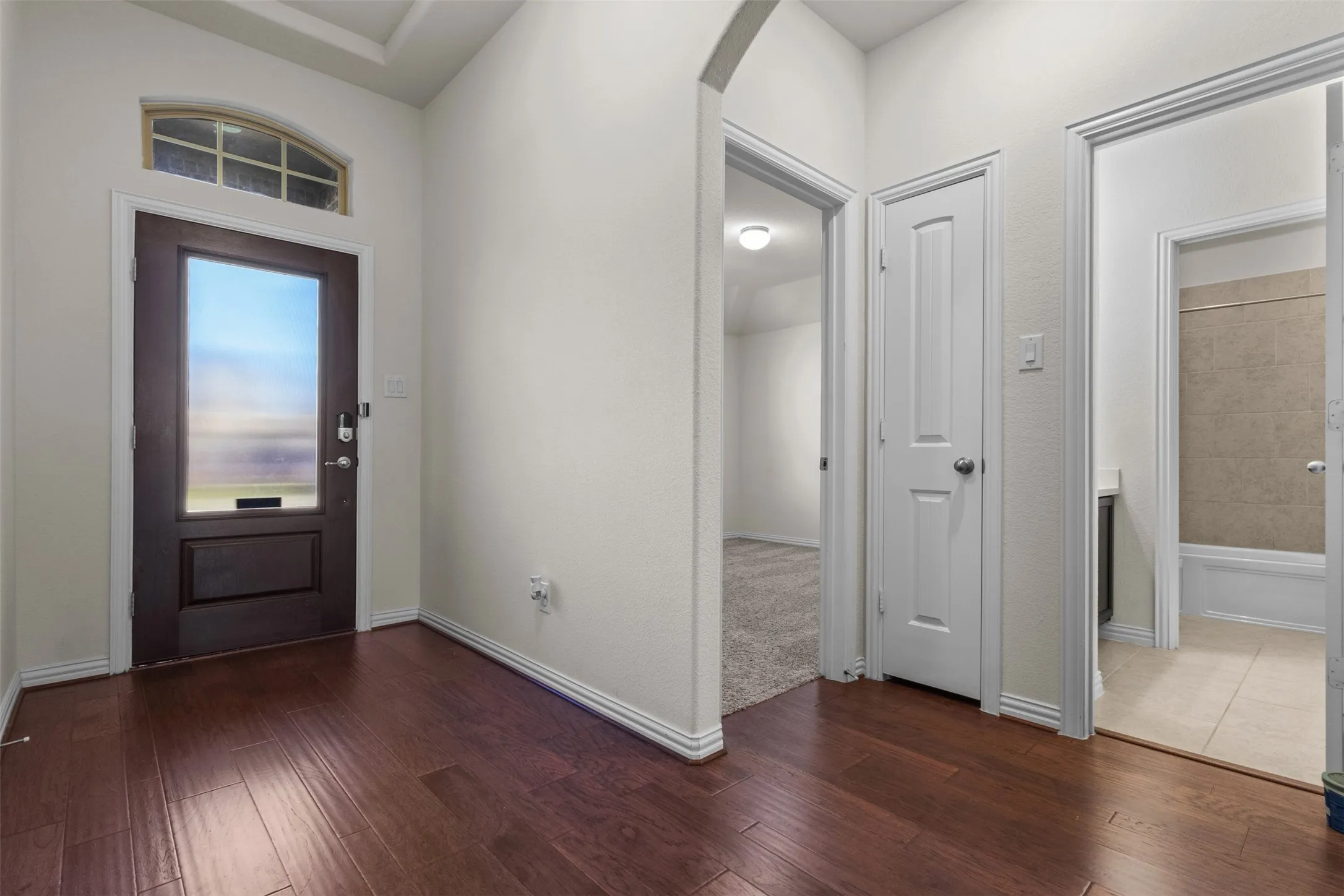 Wood-finish flooring throughout, arched entryway, white trim, and a panel door