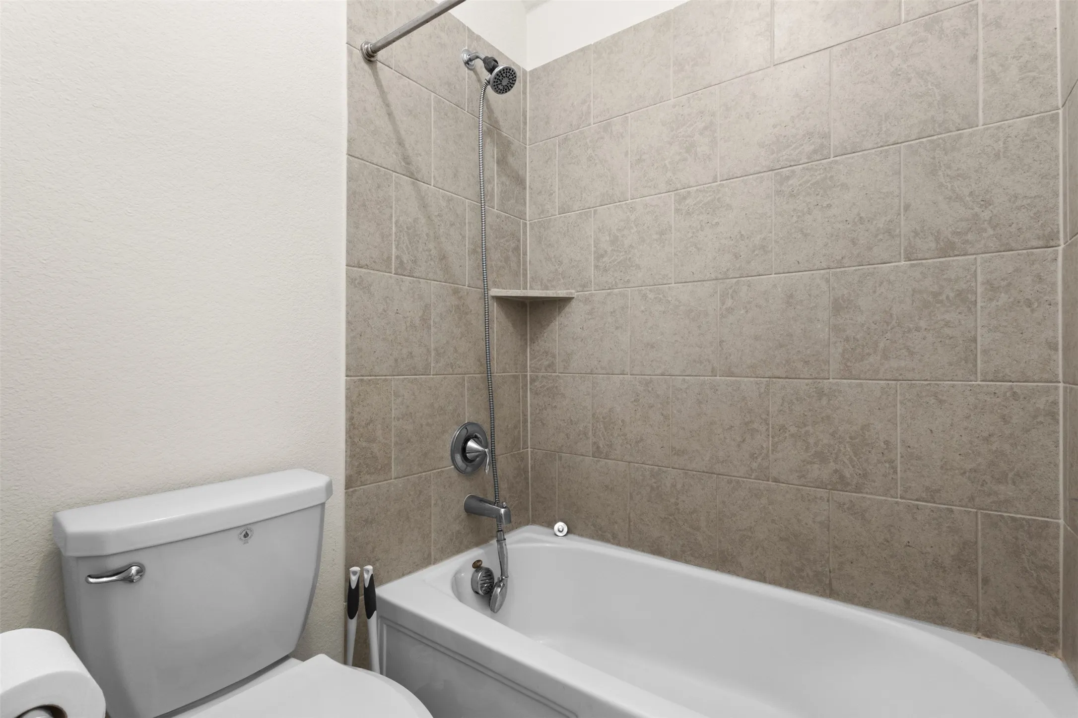 Bathtub with tiled surround, integrated shelving niche, and handheld shower fixture