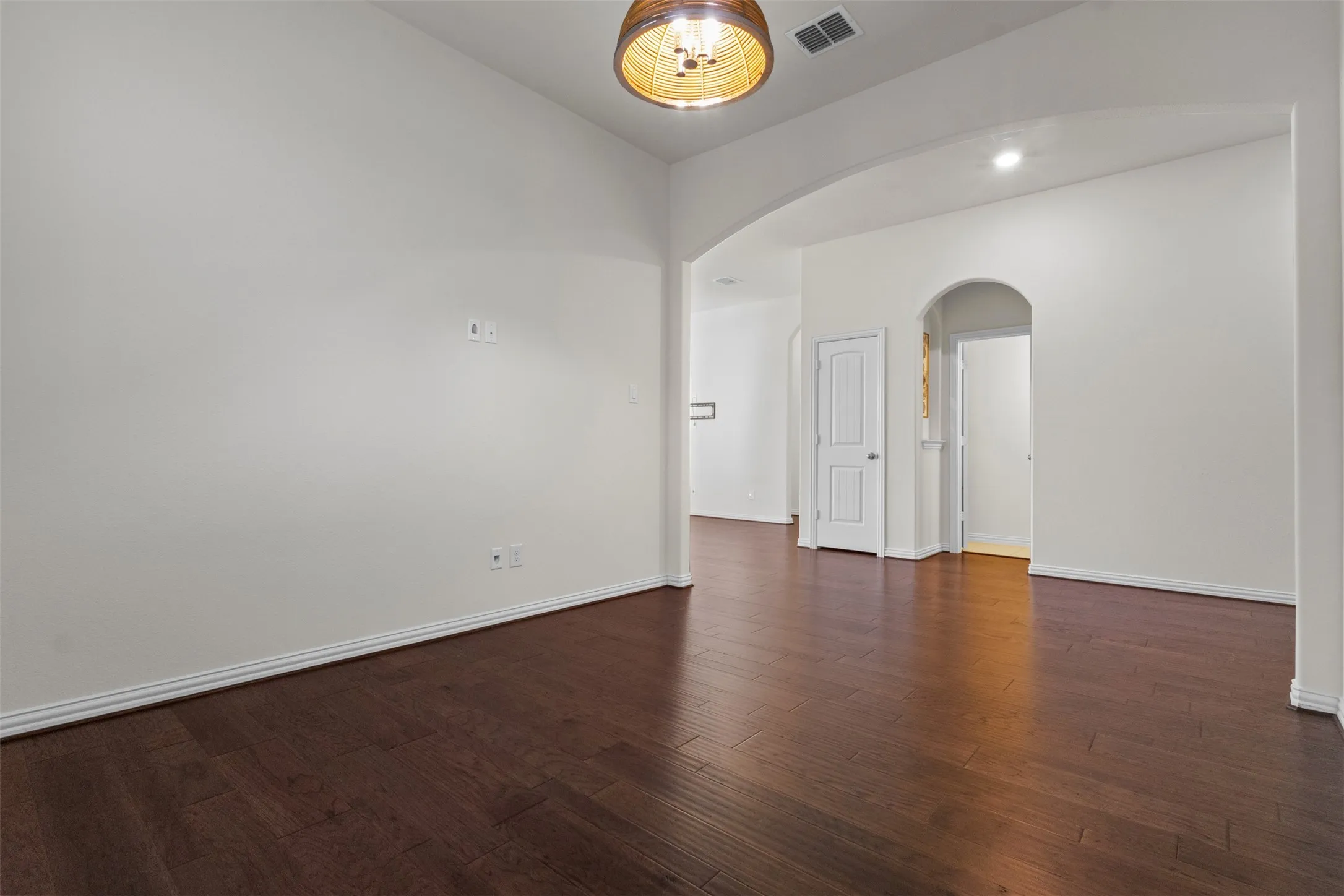 Hardwood-finish flooring throughout, white baseboards, arched doorways, and a drum-style ceiling light