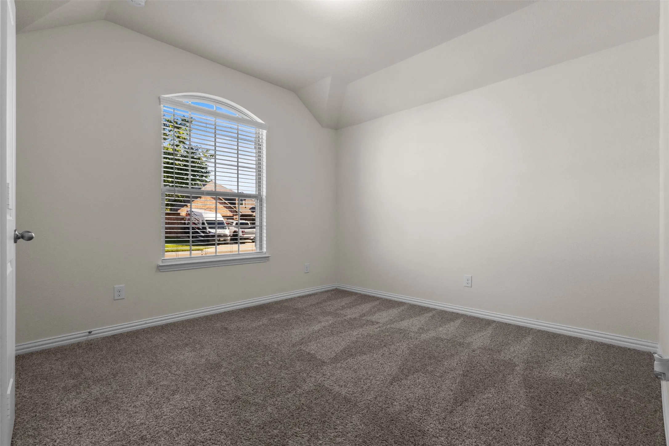 Arched window with blinds, vaulted ceiling, neutral wall paint, and patterned carpet flooring