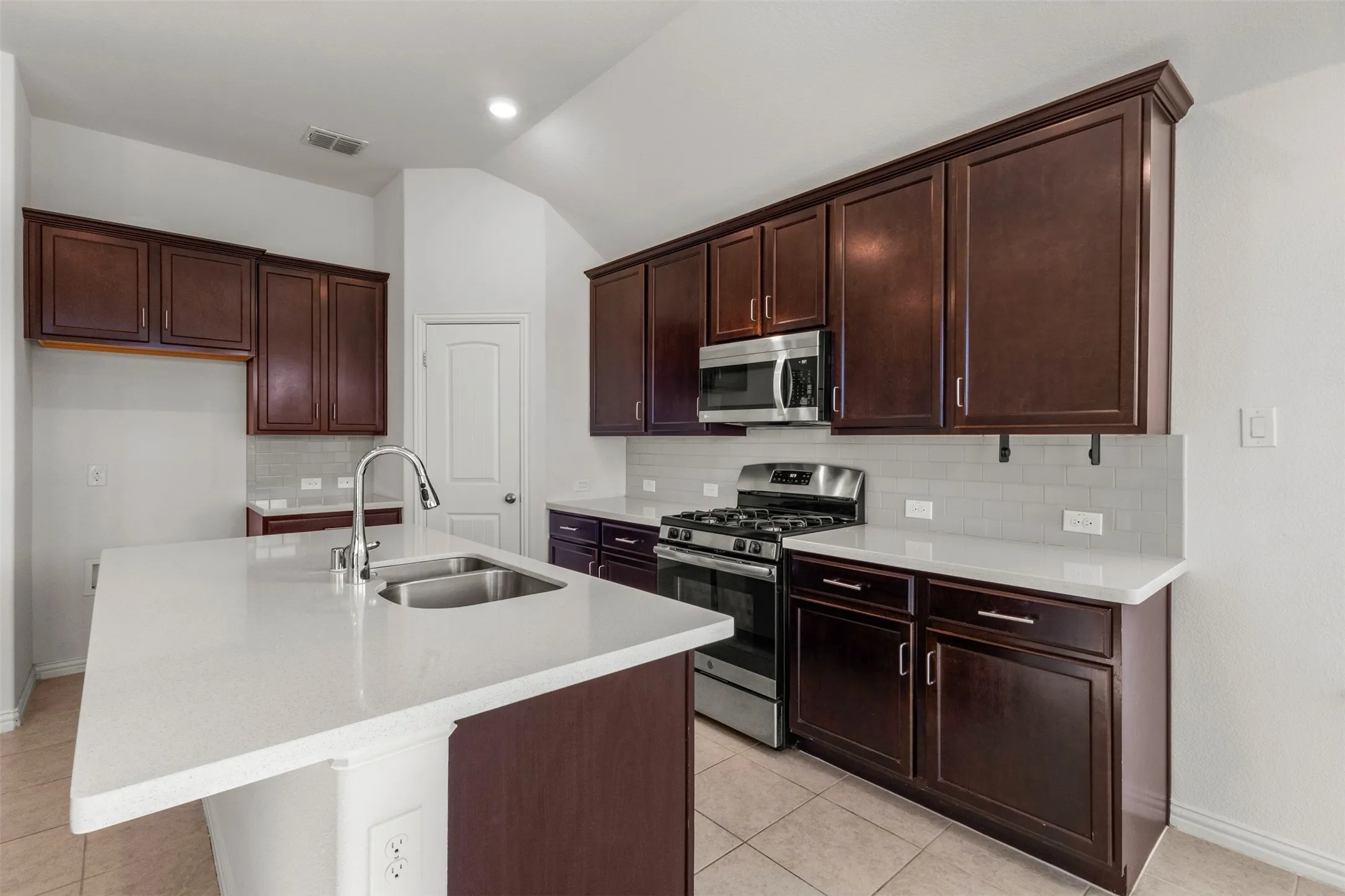 Kitchen featuring dark wood-finish cabinetry, white countertops, tile flooring, and a stainless steel gas range