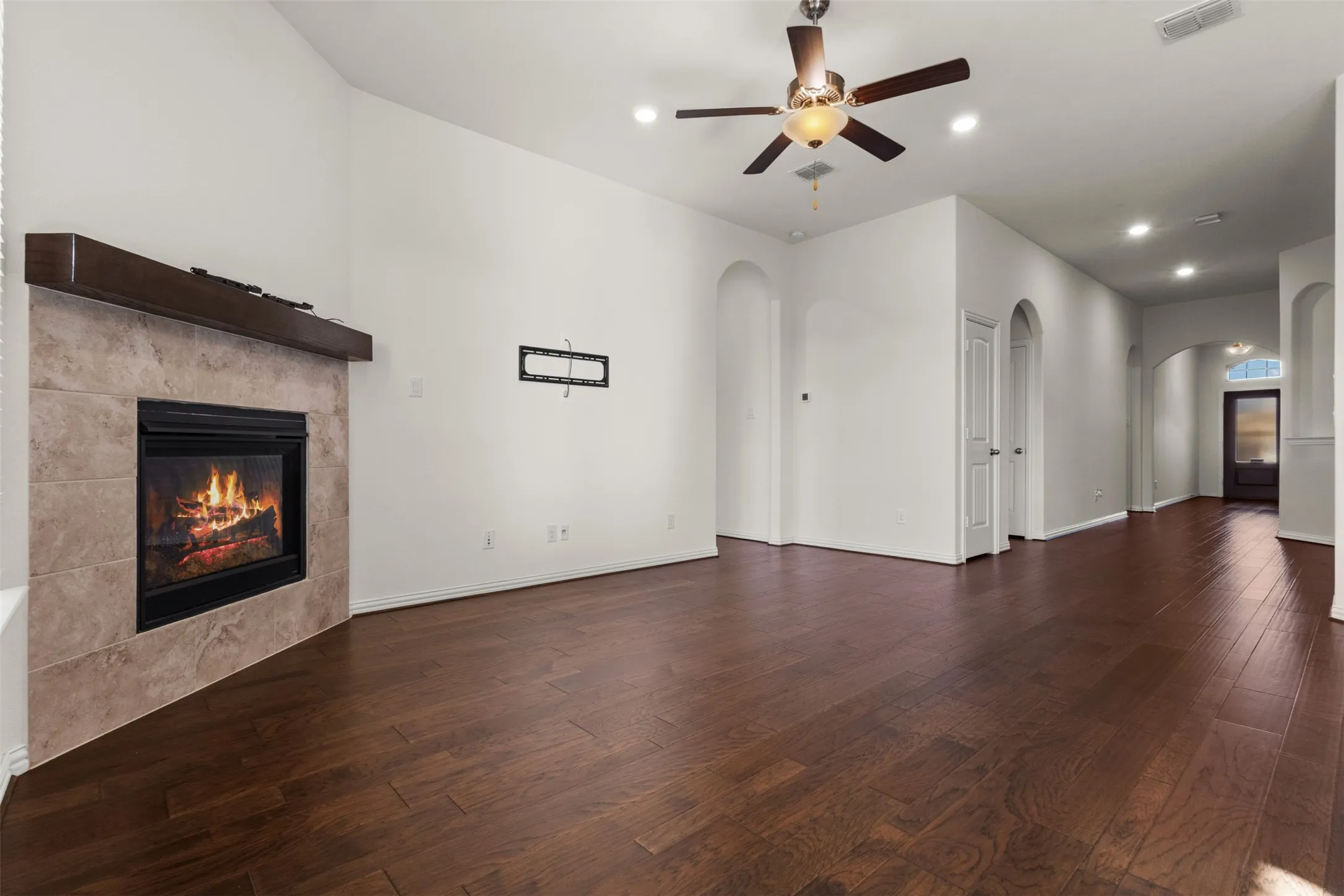 Spacious living area featuring wood-finish flooring, a tiled fireplace with a wood mantle, recessed lighting, and an overhead ceiling fan