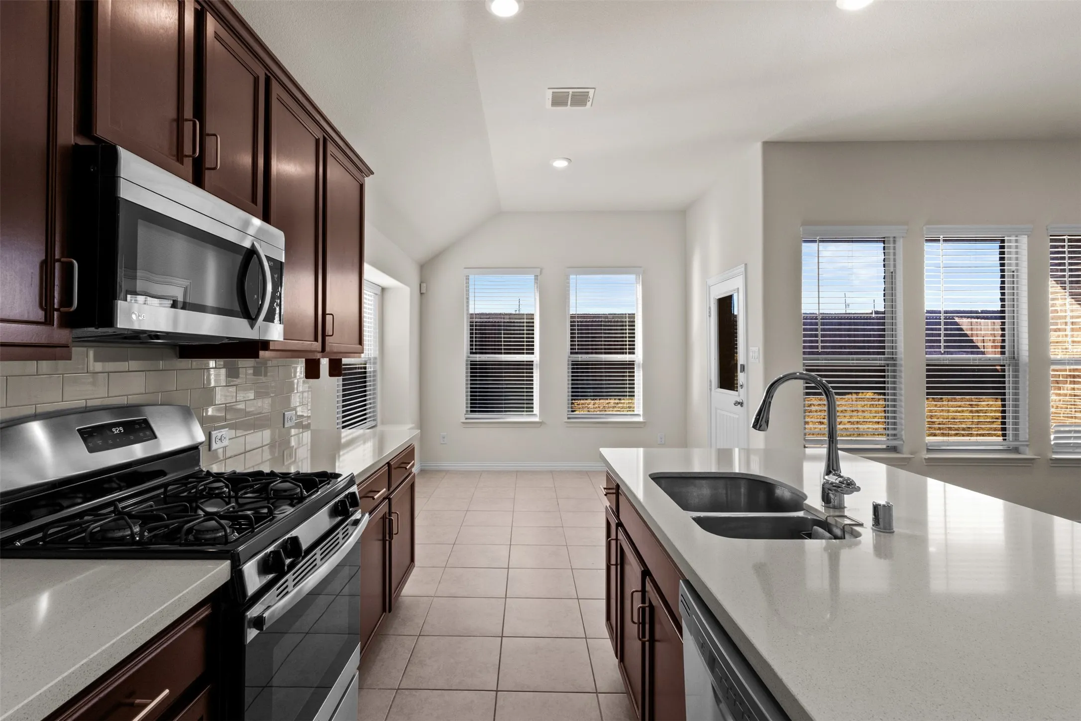 Kitchen with dark wood-finish cabinetry, stainless steel appliances, light-toned countertops, tile flooring, and a subway tile backsplash