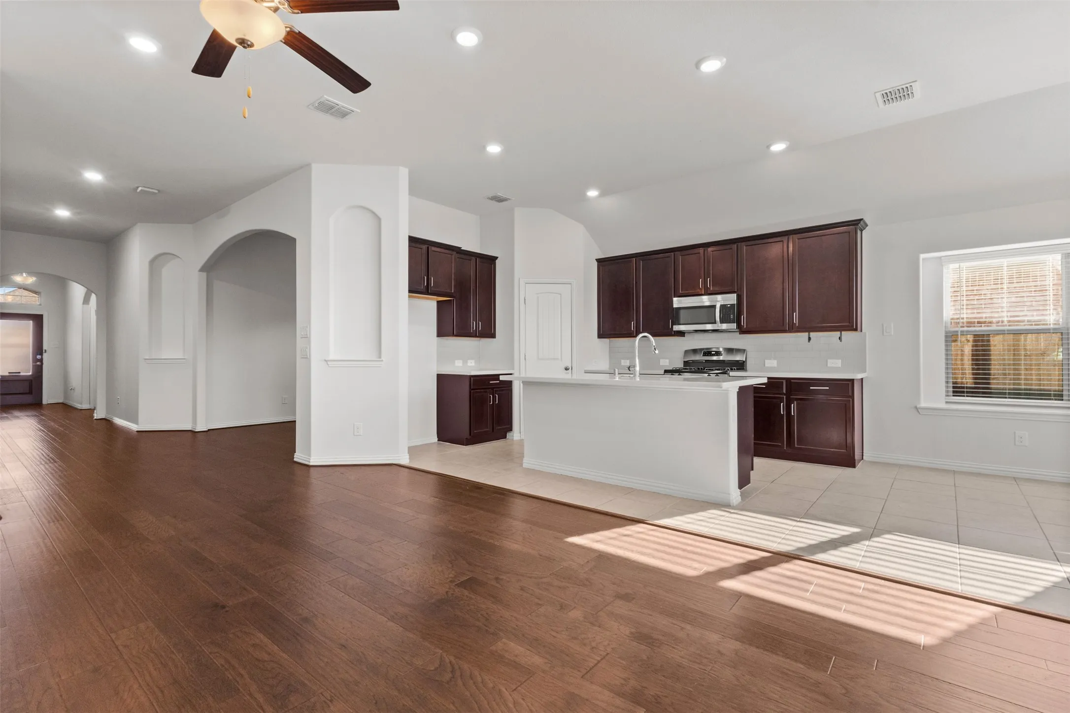 Wood-finish flooring throughout, archways, recessed lighting, ceiling fan, and kitchen island with built-in sink