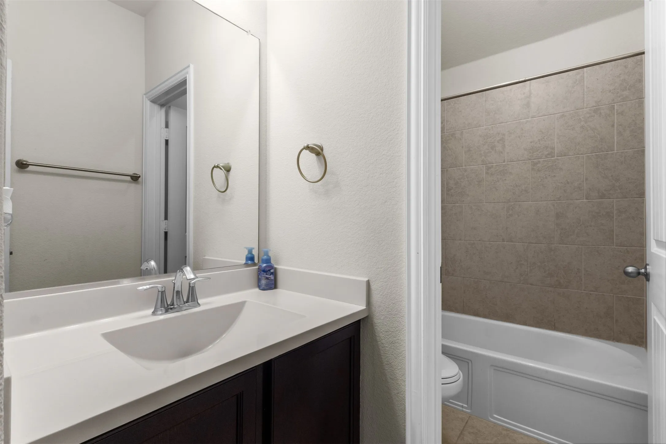 Vanity with an integrated sink and countertop, dark wood-finish cabinetry, and a full-width mirror