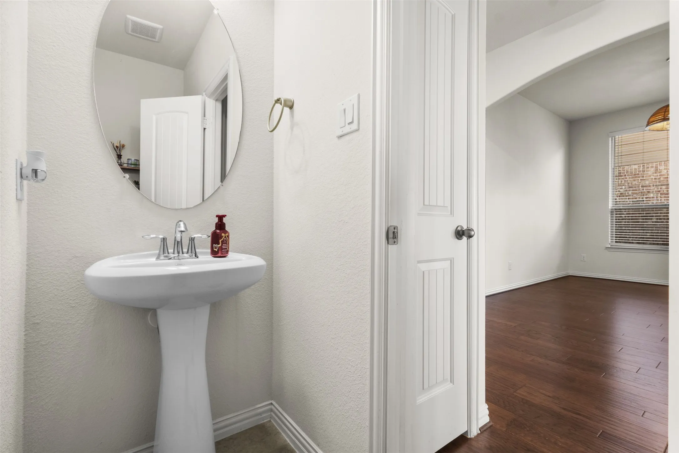 Pedestal sink with chrome faucet, oval wall mirror, and wood-finish flooring