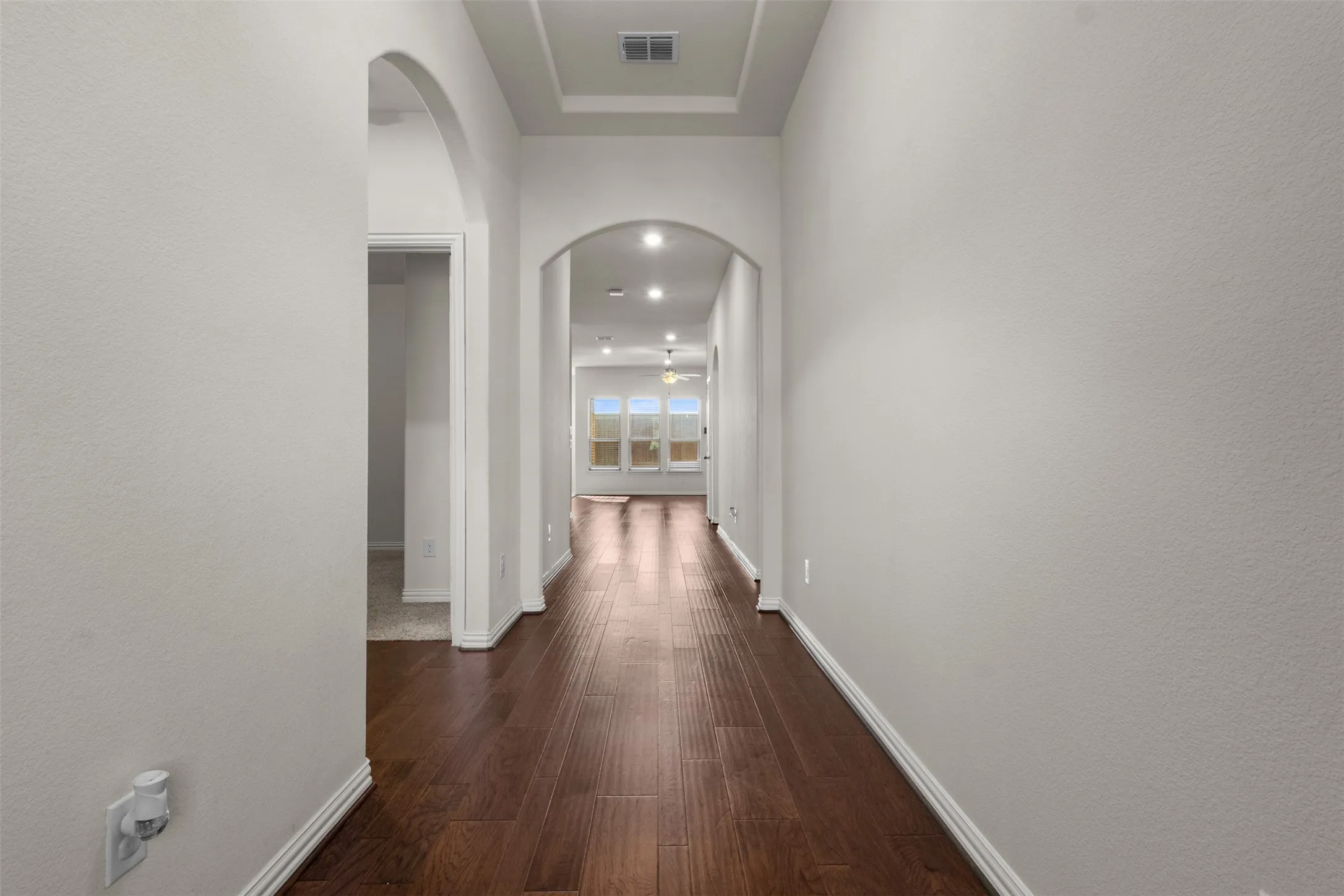 Archways define the hallway with wood-finish flooring, recessed lighting, and a tray ceiling detail