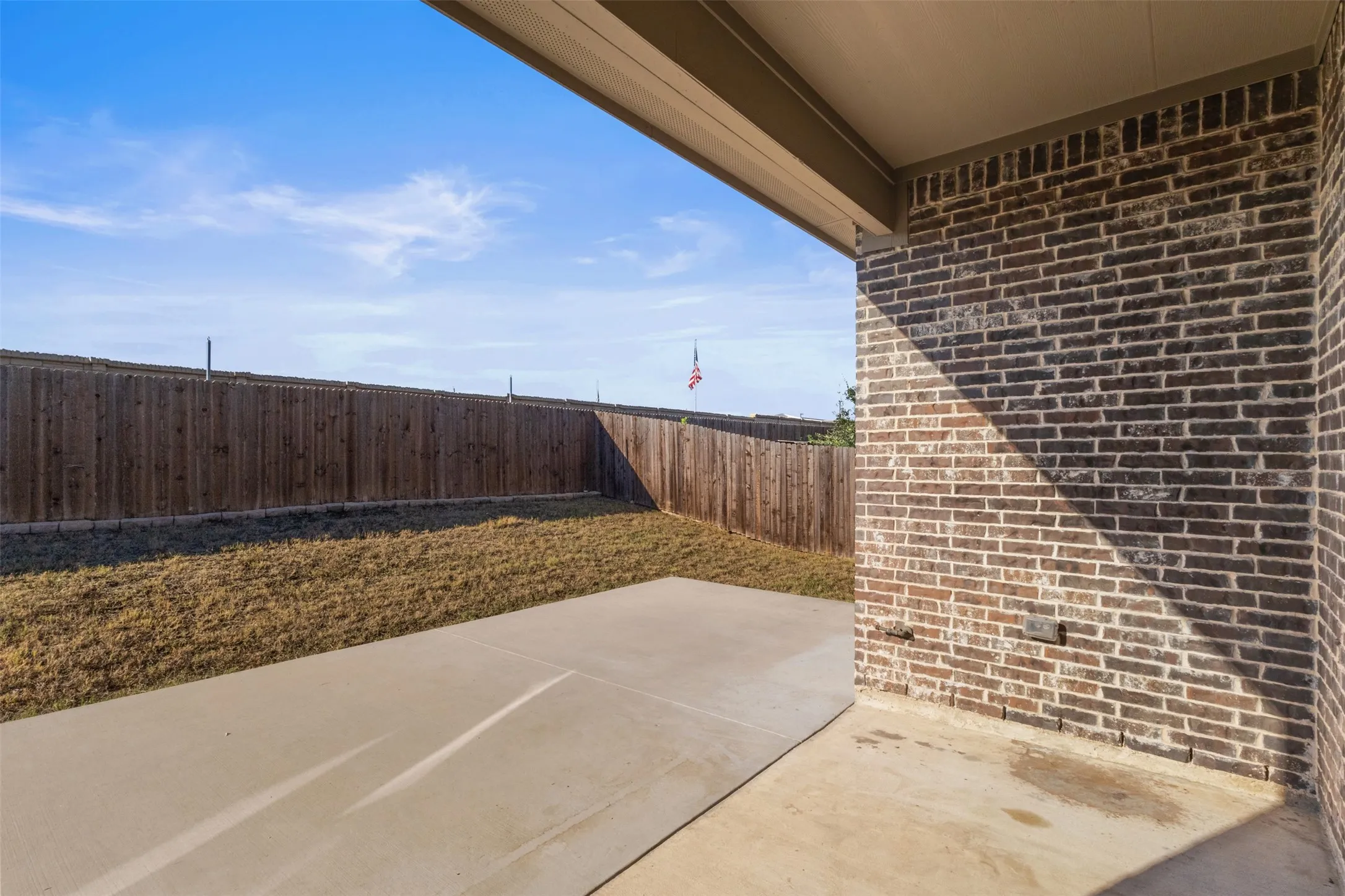 Covered patio with a concrete surface, brick exterior wall, and wood privacy fence