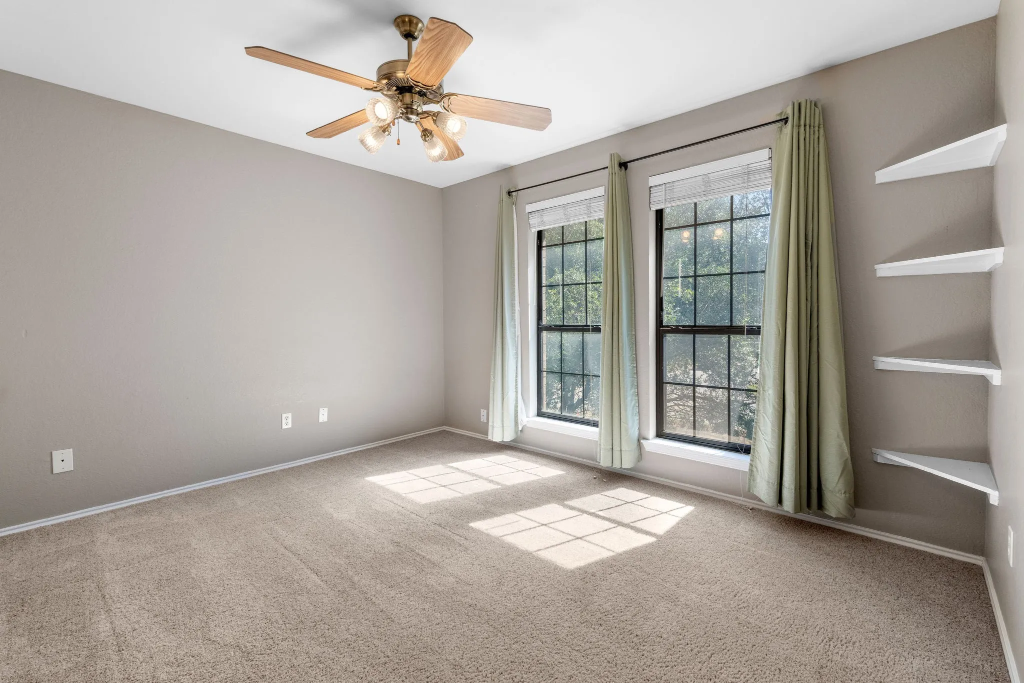Bedroom with ceiling fan, double windows overlooking front yard and corner shelving.
