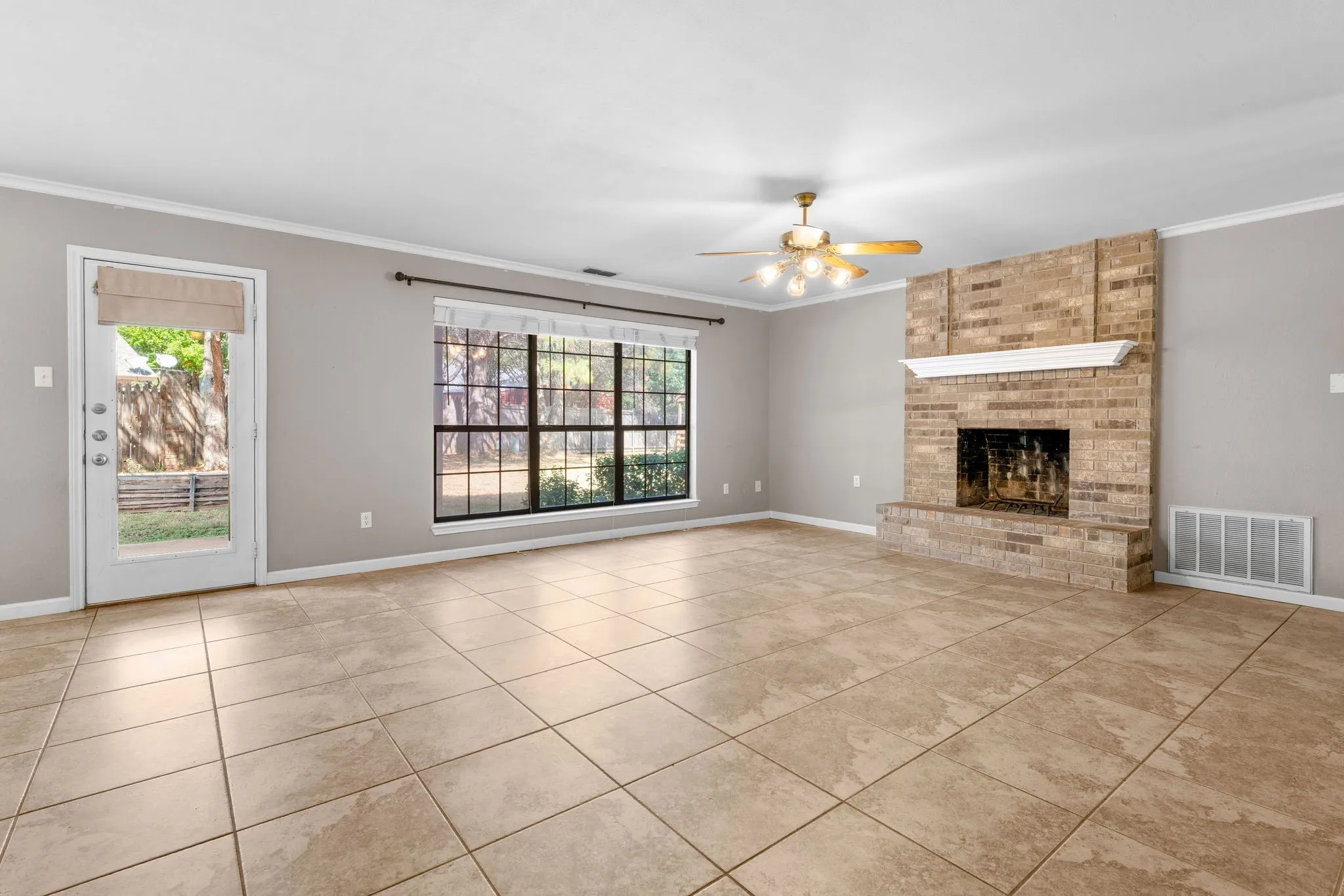 Living room with brick fireplace, triple windows, and large 18" tile floors.