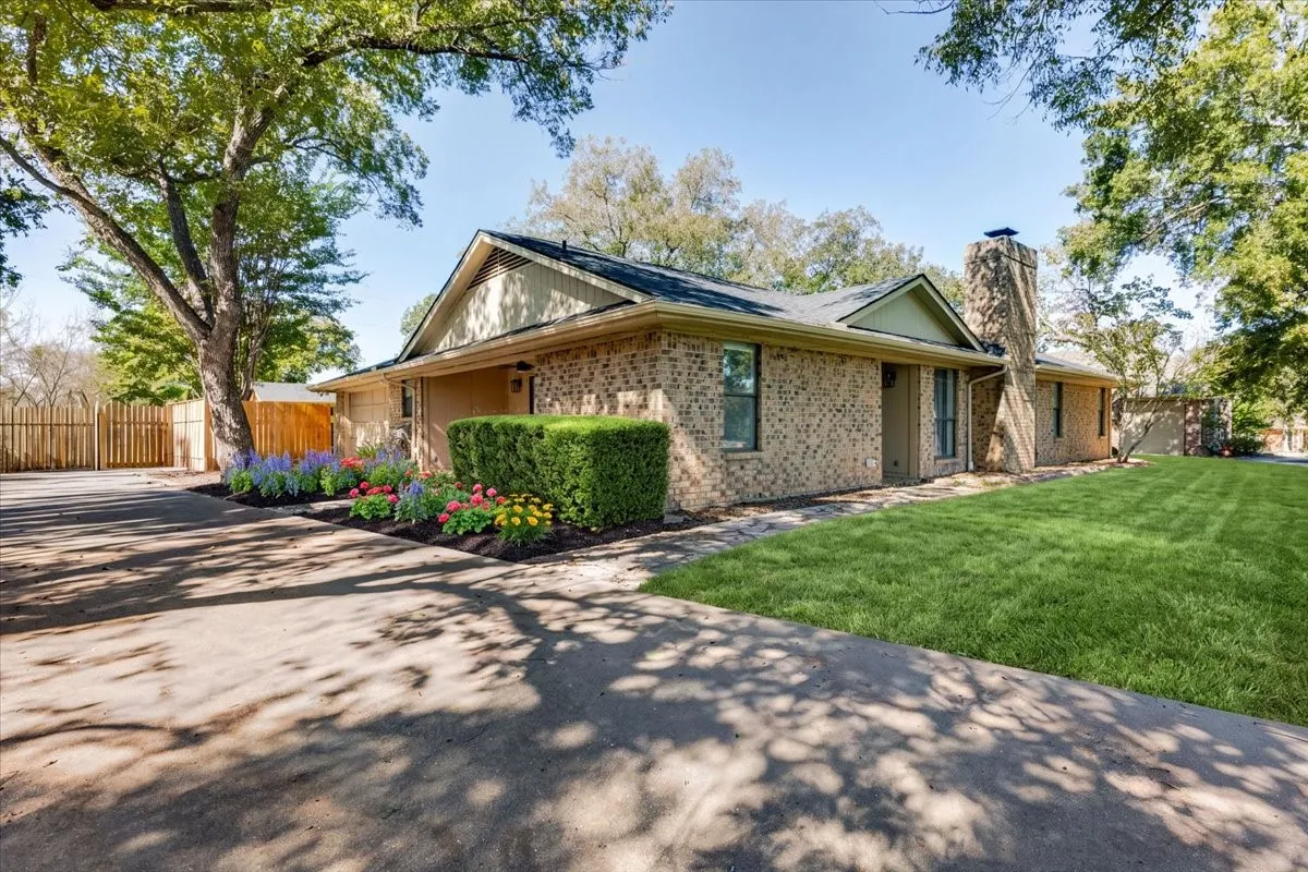 Brick exterior with a prominent stone (chimney, established trees, vibrant landscaping, and a well-maintained lawn (Lawn enhanced with AI for greenness)