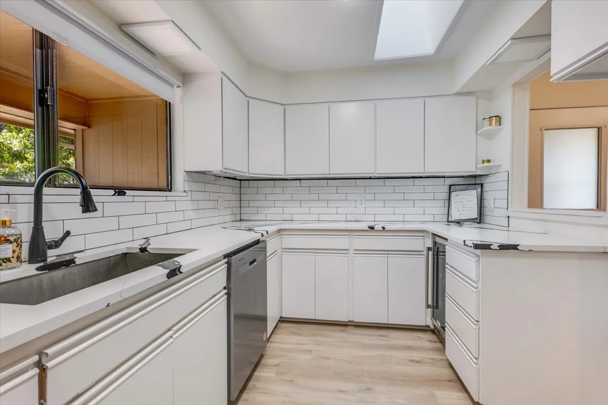 White cabinetry with solid surface countertops, subway tile backsplash, a skylight, and wood-finish flooring