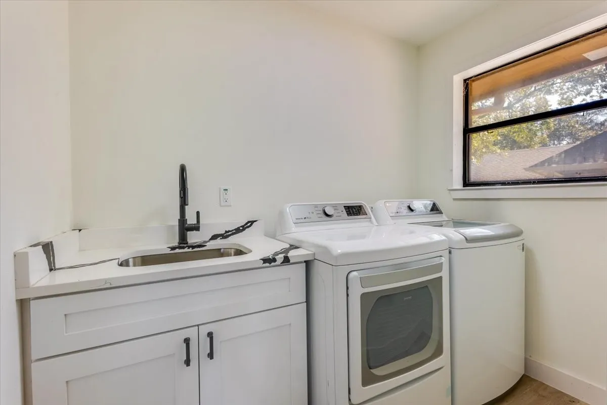 Laundry area featuring a utility sink with a matte black faucet, white cabinetry, and a window