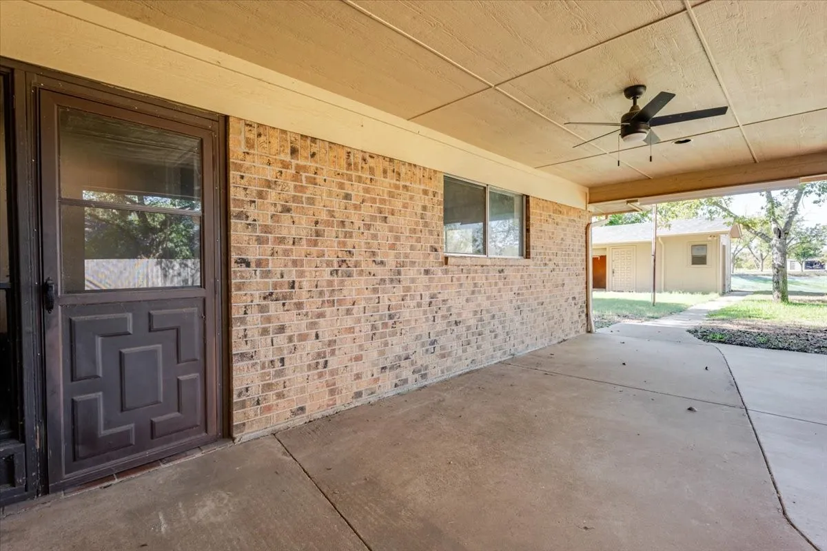 Expansive covered patio featuring a concrete surface, brick wall, and ceiling fan