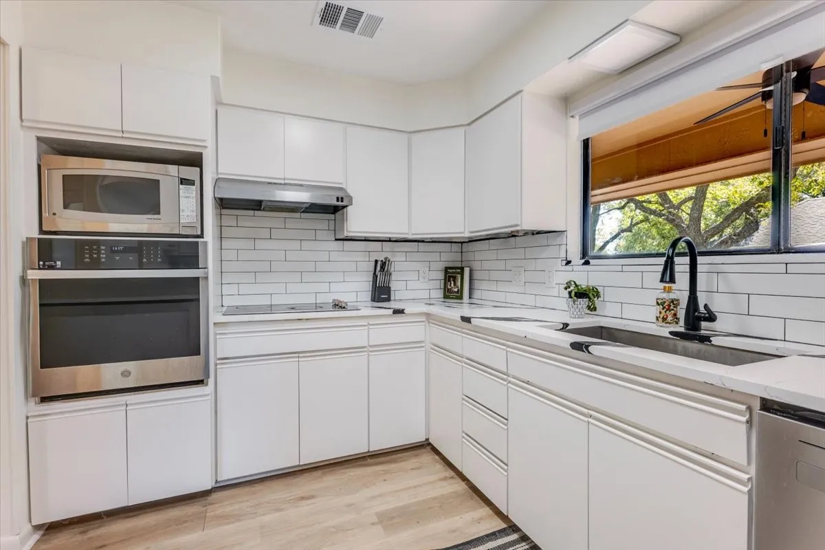 White cabinetry with integrated stainless steel appliances, subway tile backsplash, and light-toned countertops