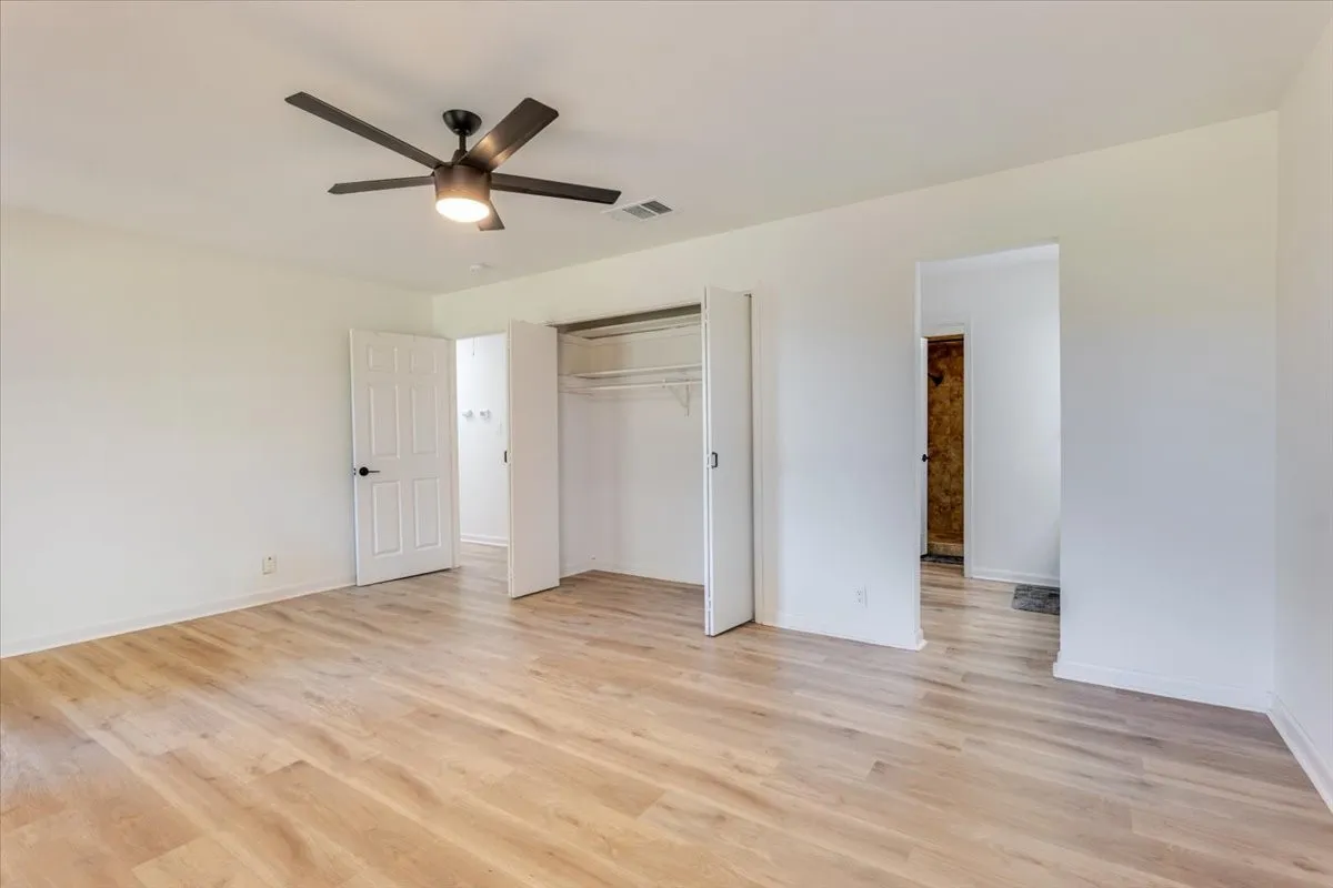 Expansive room featuring wood-finish flooring, a contemporary ceiling fan, and a built-in closet with bifold doors