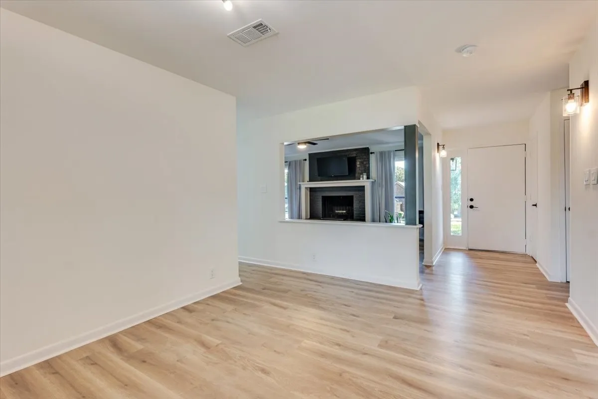 Light wood-finish flooring throughout, a white entry door with a vertical glass panel, and two wall-mounted sconces with clear glass shades