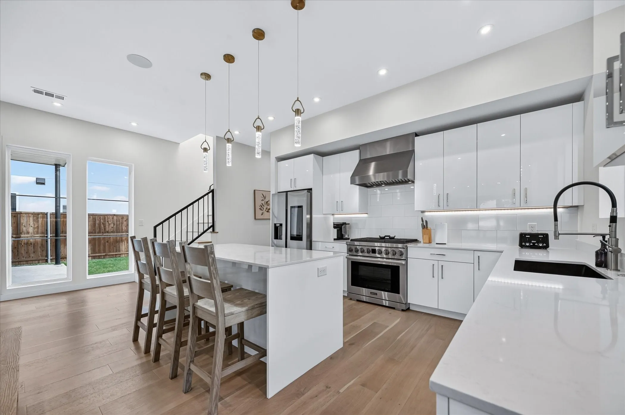Modern kitchen featuring glossy white cabinetry, stainless steel appliances, a center island with seating, and light wood-finish flooring