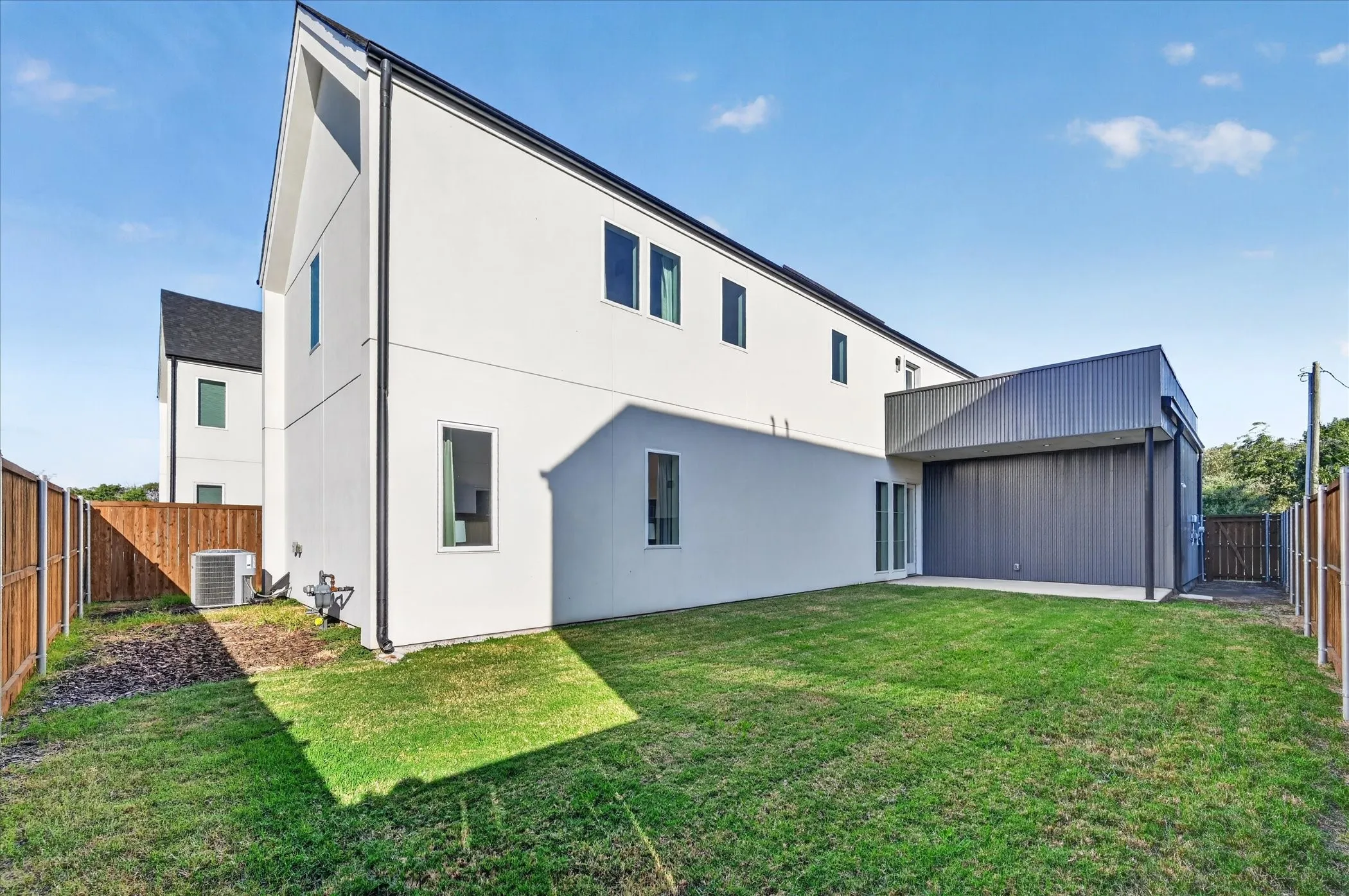 Modern exterior architecture with a steep-pitched roofline, white stucco siding, and a corrugated metal accent wall