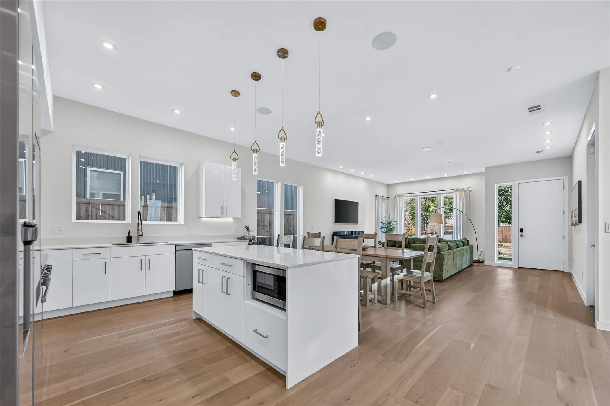 Bright open-concept living area featuring wood-finish flooring, recessed lighting, white cabinetry, and a kitchen island with seating