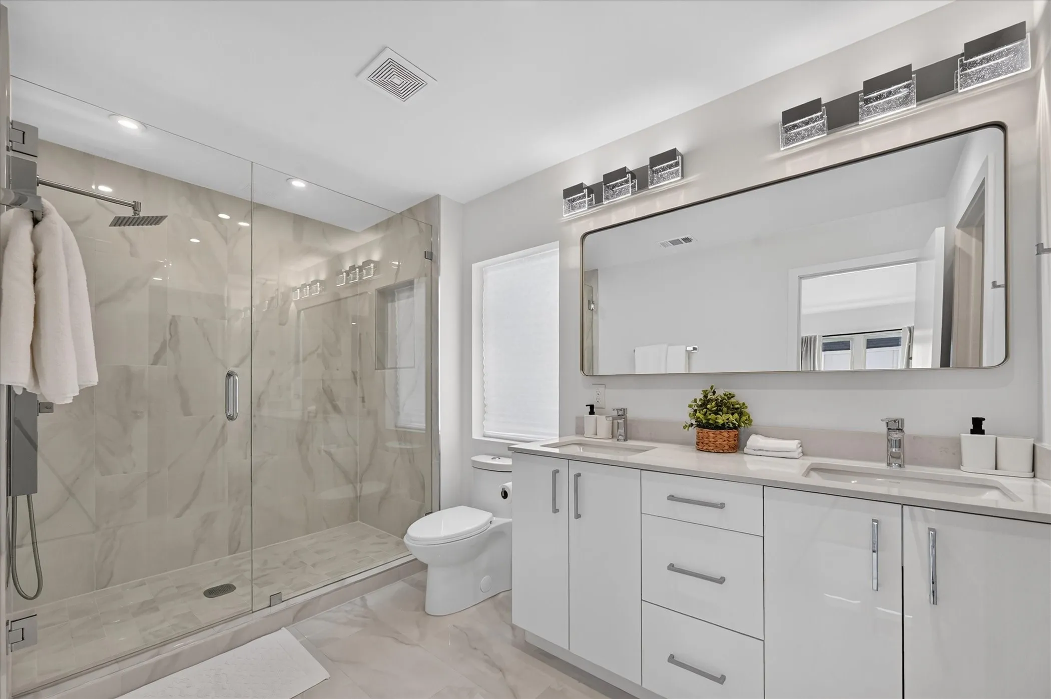 Dual vanity with integrated sinks and white cabinetry, expansive frameless mirror, and overhead decorative lighting