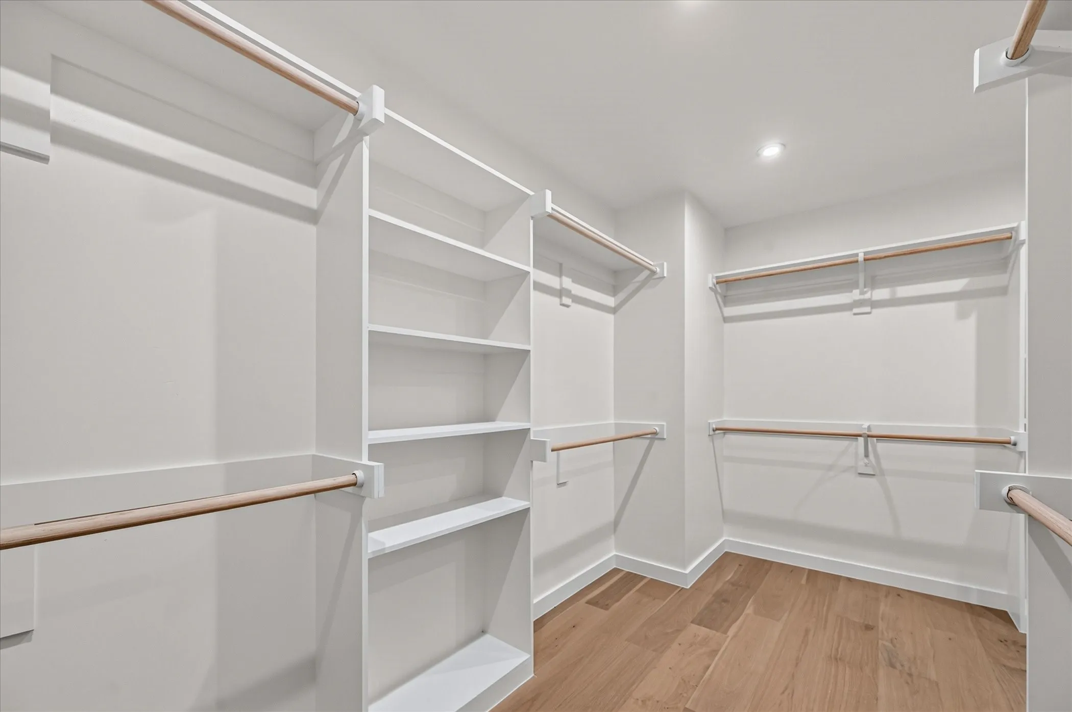 Walk-in closet featuring built-in shelving, multiple hanging rods, recessed lighting, and wood-finish flooring