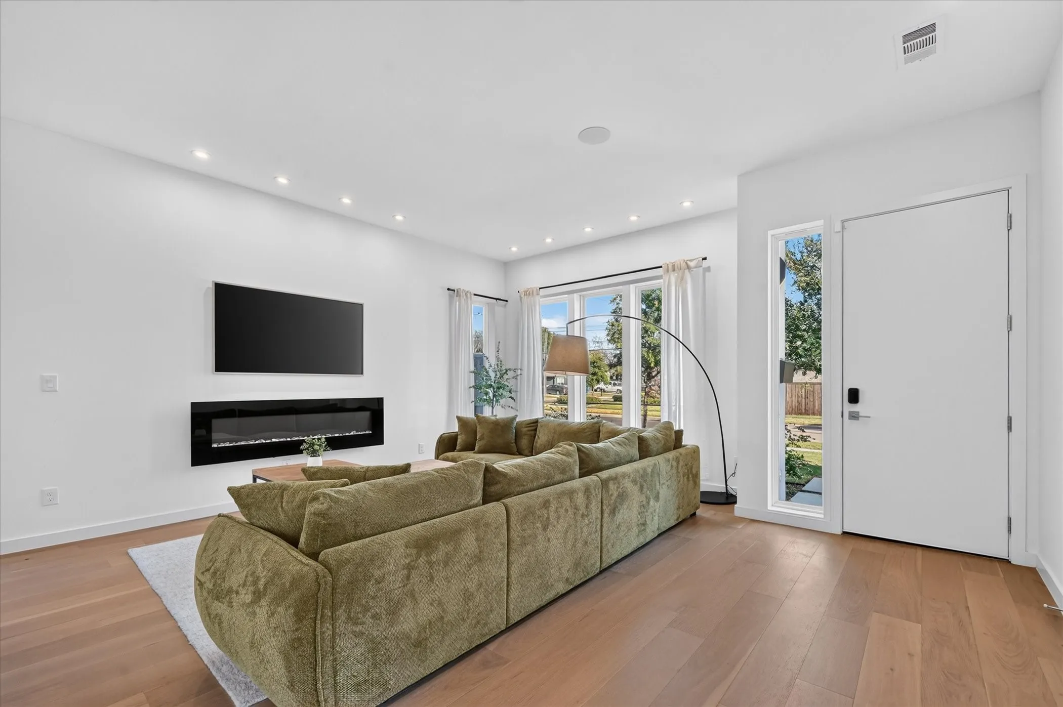 Recessed lighting, wood-finish flooring, large windows, wall-mounted electric fireplace, and a side-light entry door