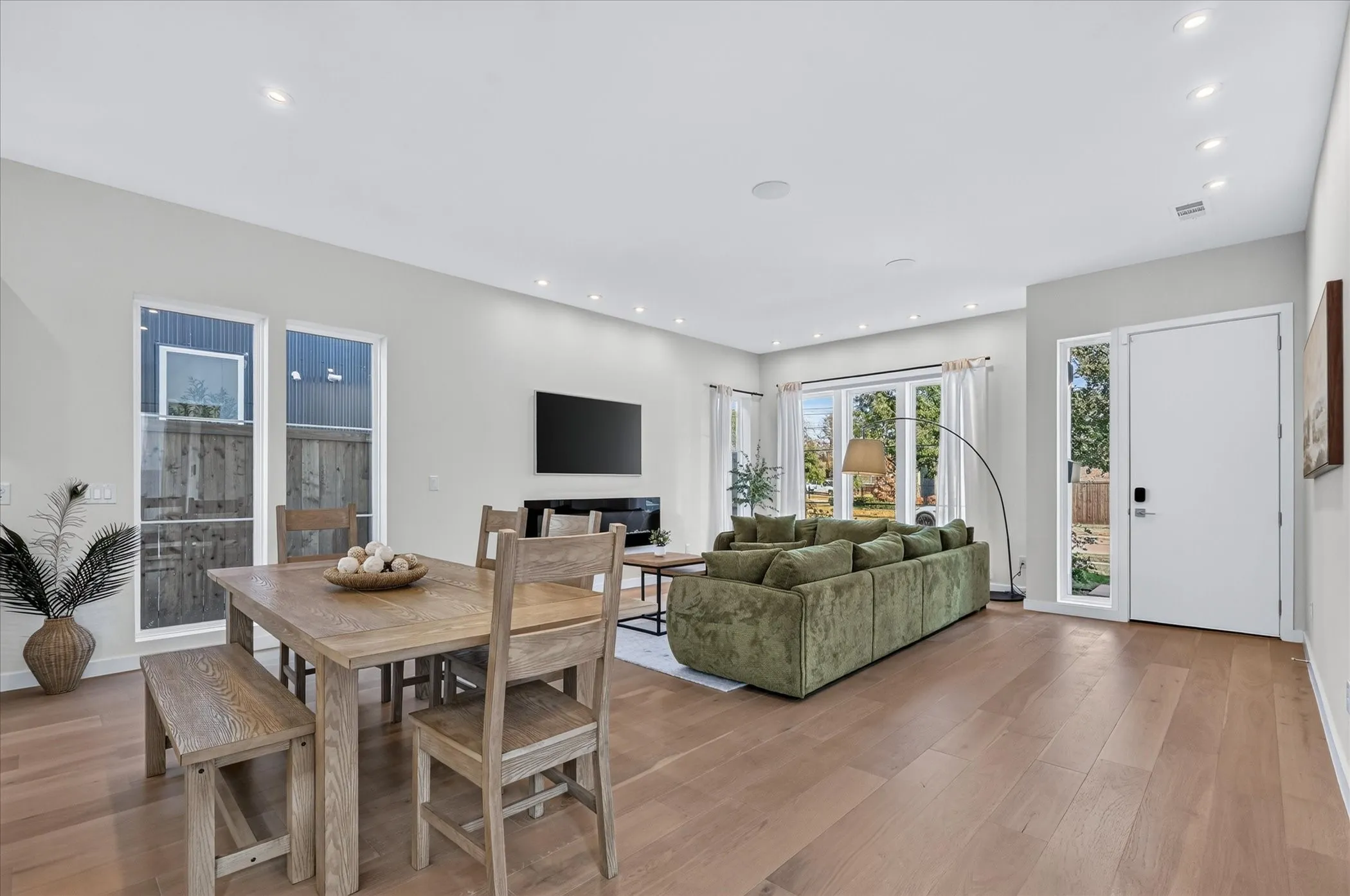 Spacious open-concept living area featuring wood-finish flooring, recessed lighting, expansive windows, and a built-in fireplace
