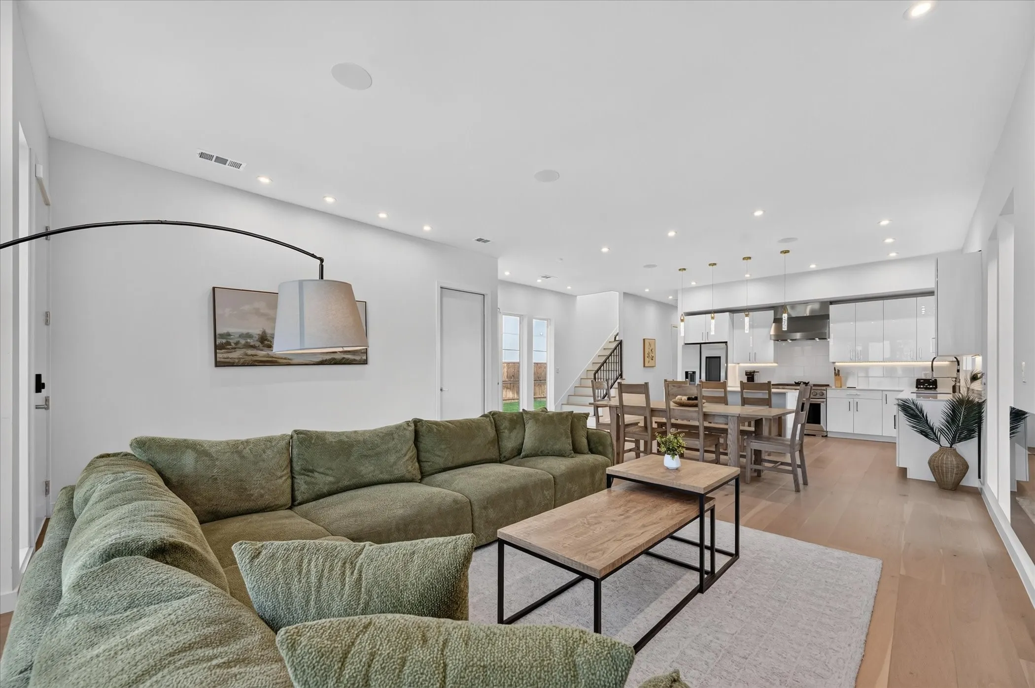Open-concept living area with wood-finish flooring, recessed lighting, and a modern kitchen featuring white cabinetry and stainless steel appliances