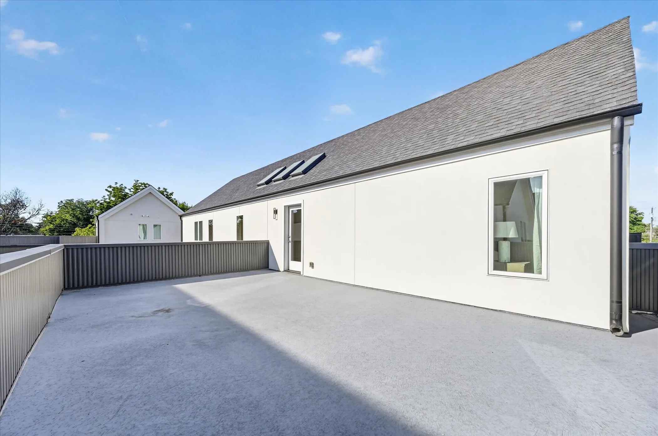 Spacious rooftop patio with concrete surfacing and contemporary slatted railings, featuring a white stucco exterior and dark shingle roofing