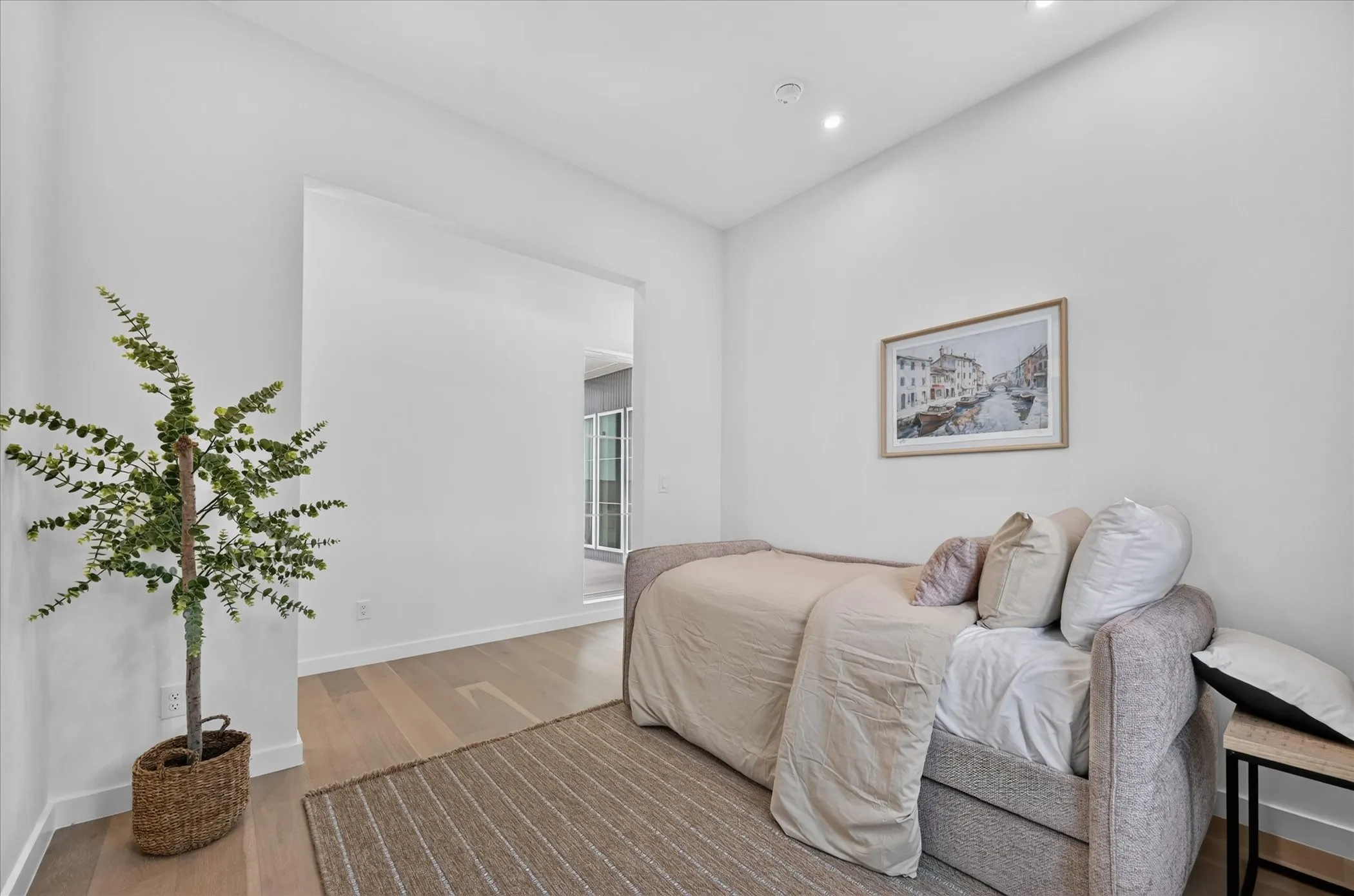 Bright secondary bedroom featuring wood-finish flooring, recessed ceiling lighting, and abundant natural light from the entry passage