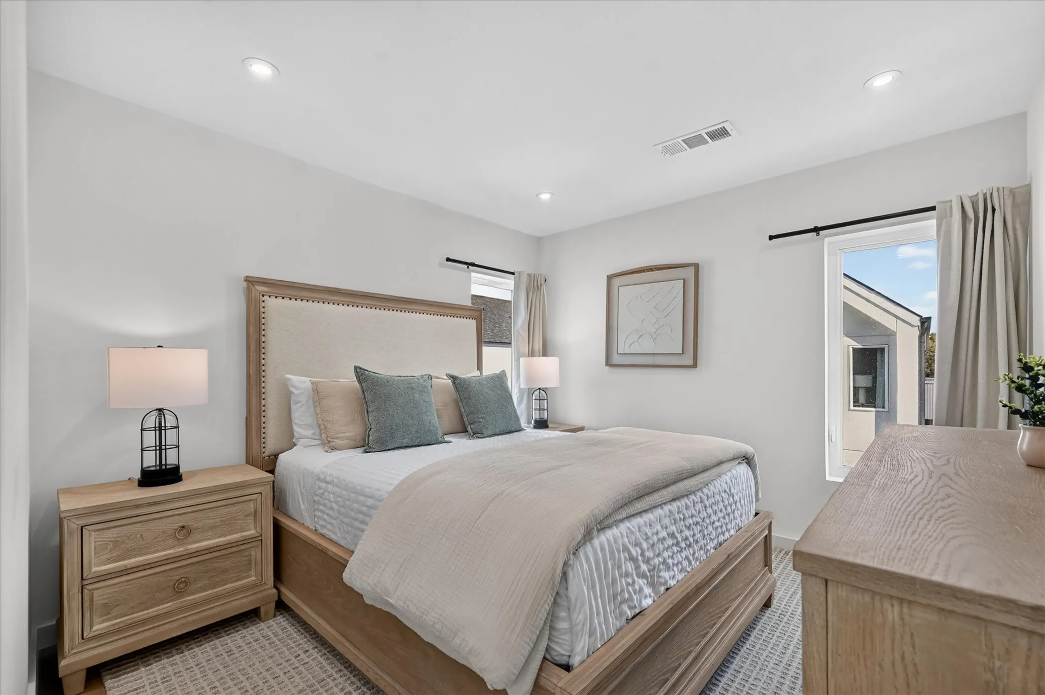 Primary bedroom featuring a wood-frame bed with nailhead trim, coordinating wood nightstands with drawer storage, recessed ceiling lighting, and large windows with neutral drapery