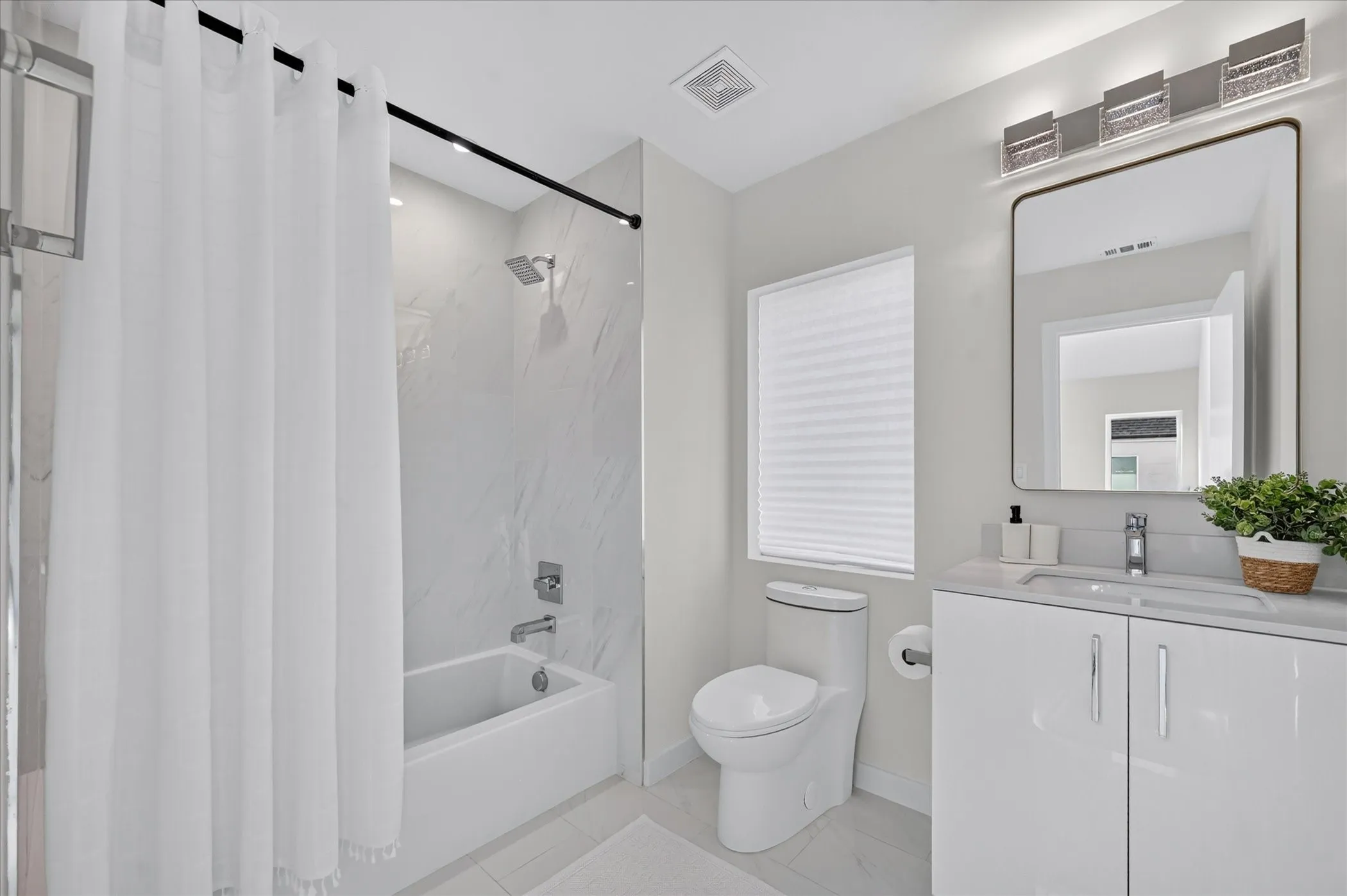 Modern bathroom featuring a floating double-vanity with white cabinetry and integrated sink, quartz countertop, framed mirror with integrated lighting, white subway tile flooring, and a separate soaking tub with glass-enclosed shower surround and chrome fixtures