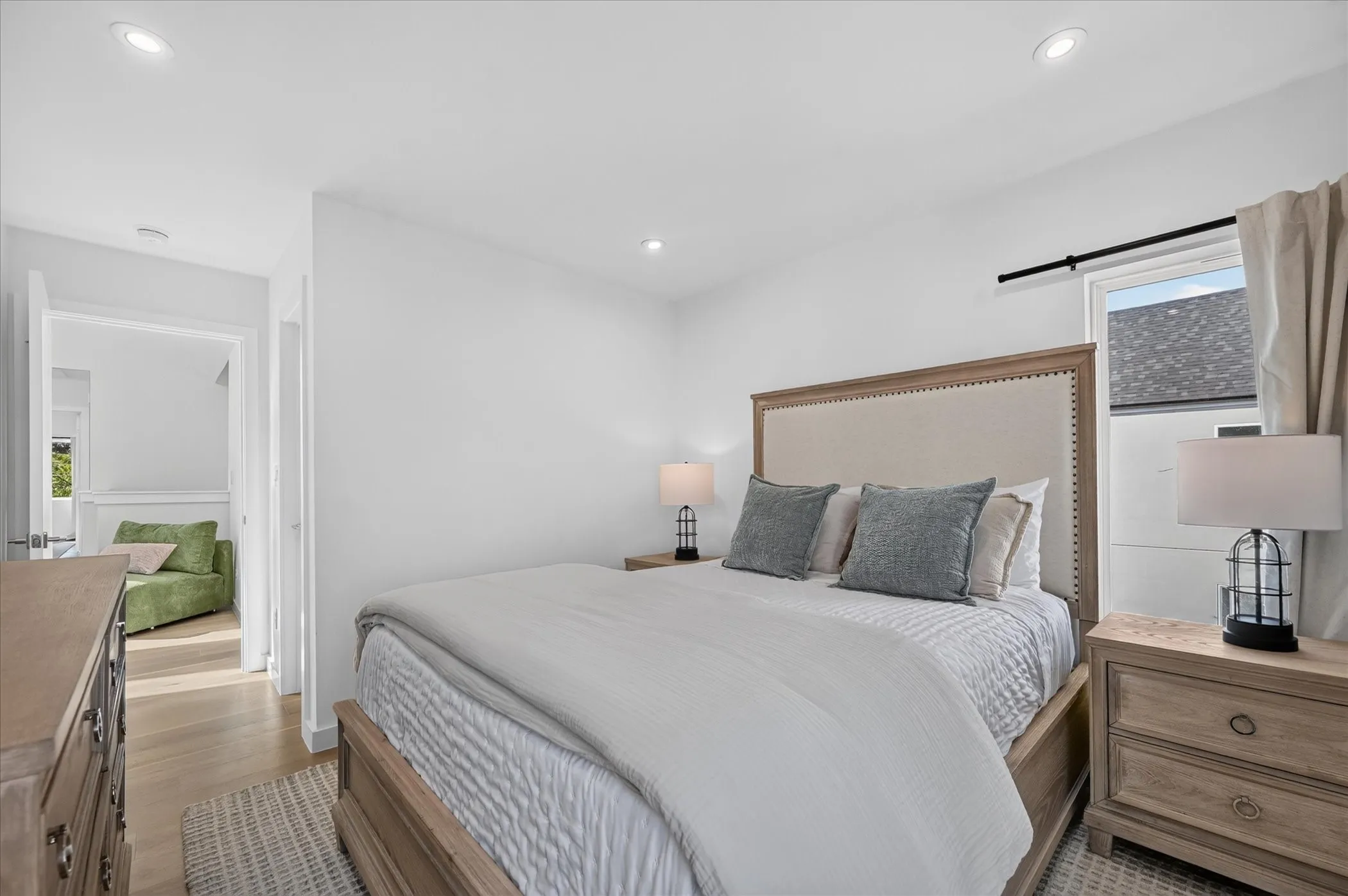 Recessed lighting, light wood-finish flooring, white walls, window with dark rod, and an open doorway