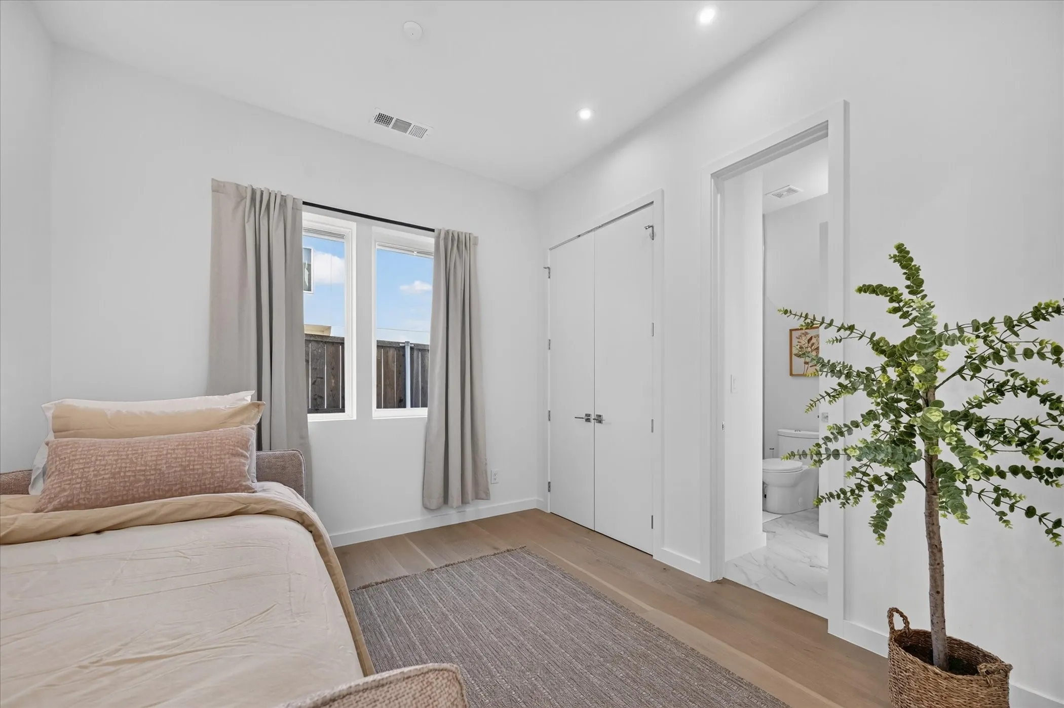 Bright secondary bedroom featuring hardwood flooring, floor-to-ceiling white closet doors, and glass-paneled French doors with thermal-pane windows